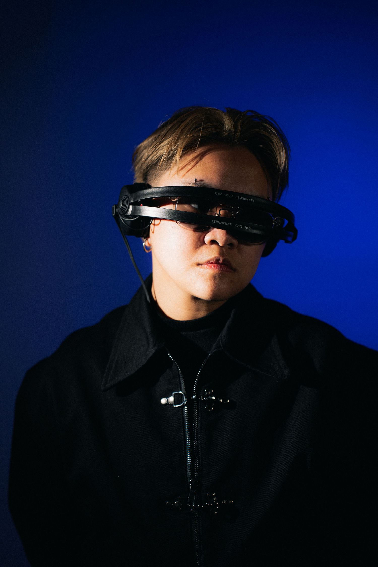 A person wearing a black jacket and futuristic virtual reality headset against a dark blue background.