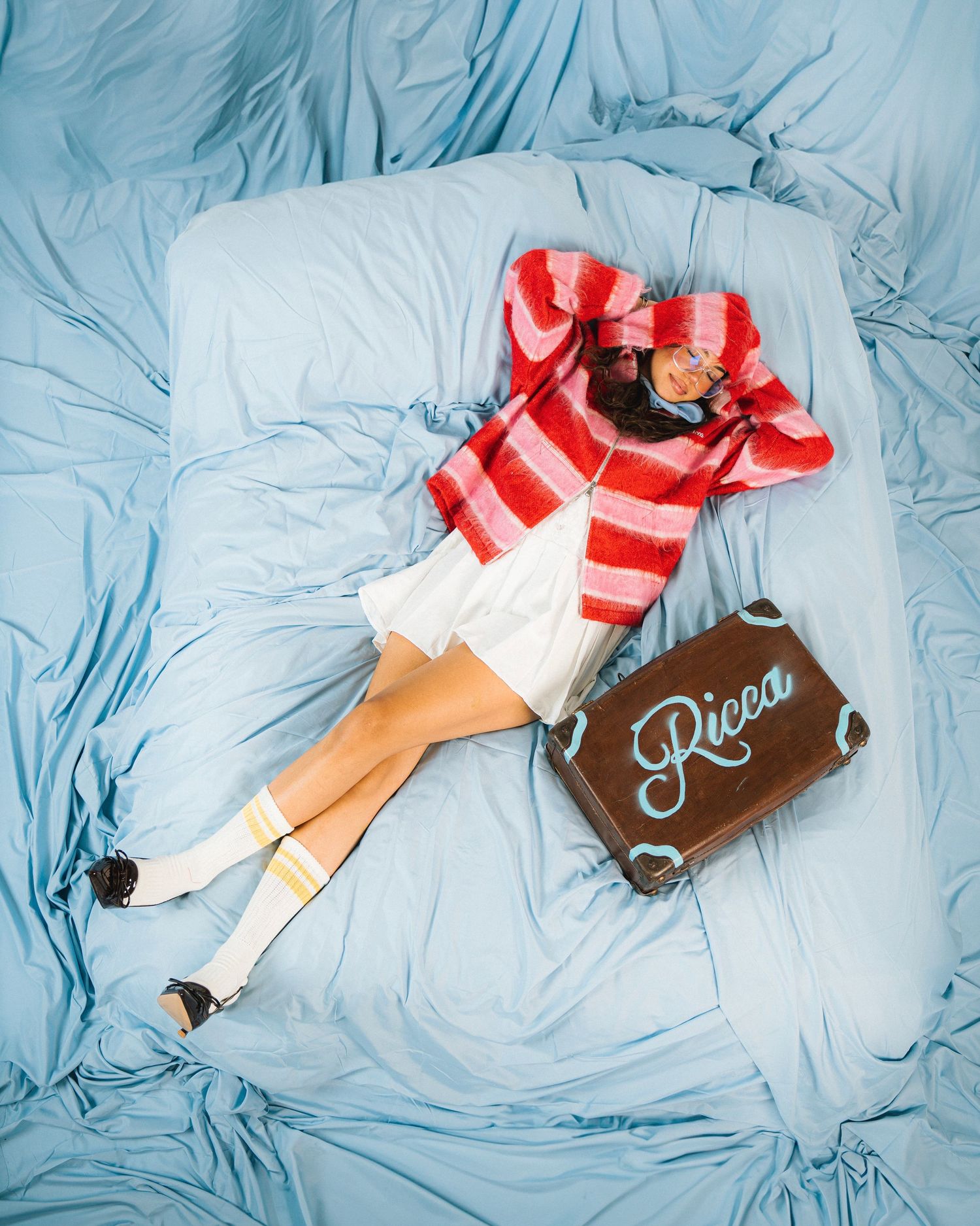 Artistic overhead shot of someone in red and white stripes lying on blue fabric with a Ricco sign.