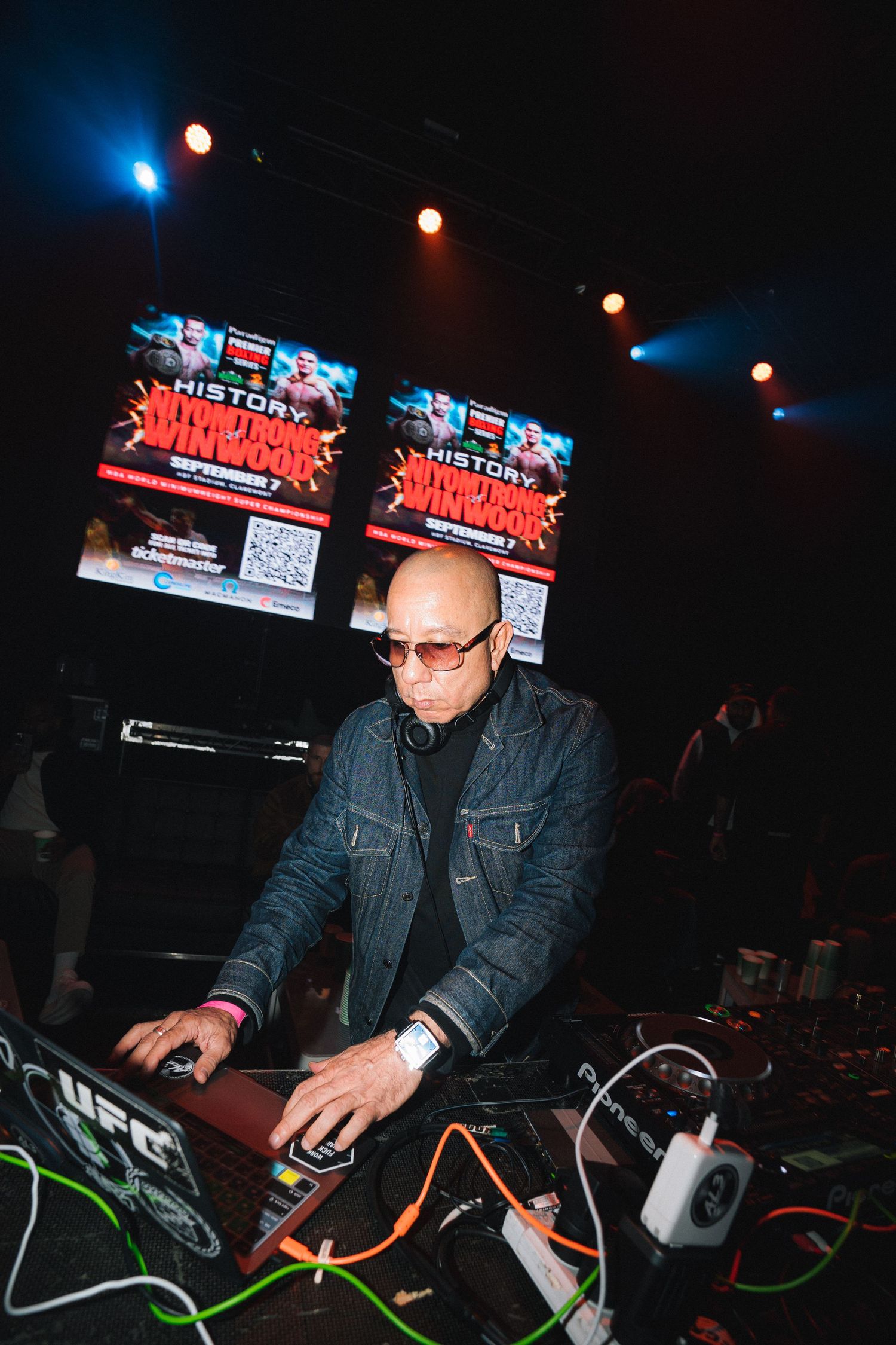 DJ performing at a nightclub event with promotional screens displaying event graphics in the background.