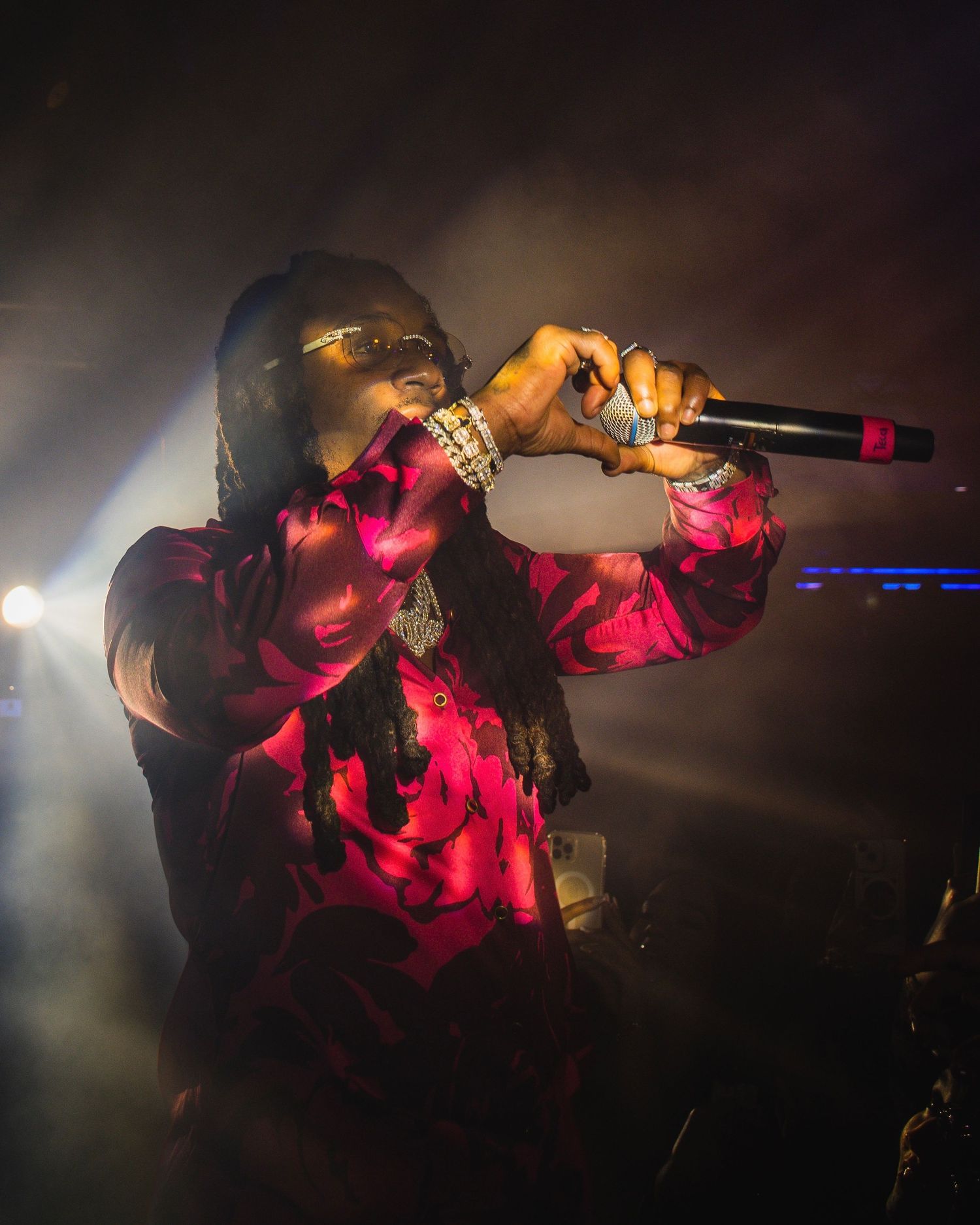 Artist in red illuminated outfit performs on stage with microphone and dramatic lighting effects.