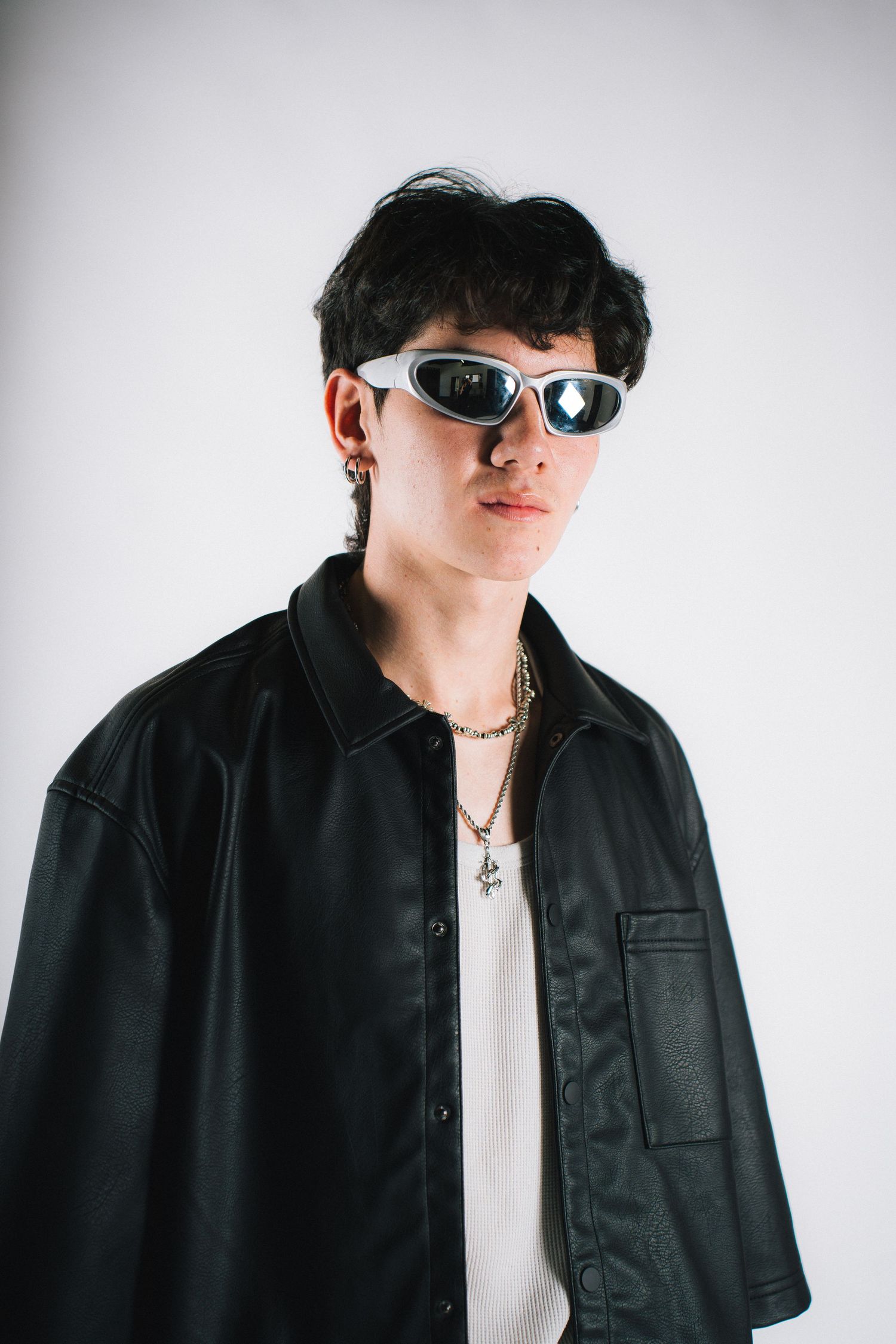 Stylish portrait of someone wearing dark sunglasses, a black button-up shirt and white undershirt with gold necklace.
