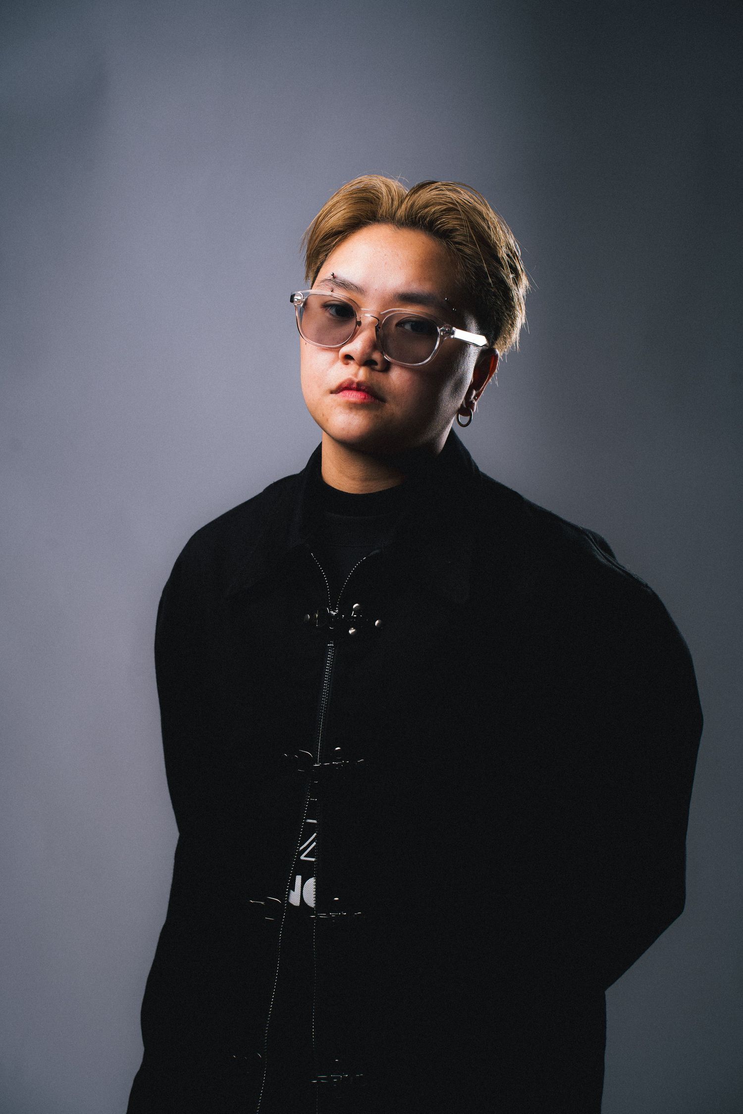 Person wearing glasses and a black winter coat poses against gray backdrop in dramatic studio lighting.