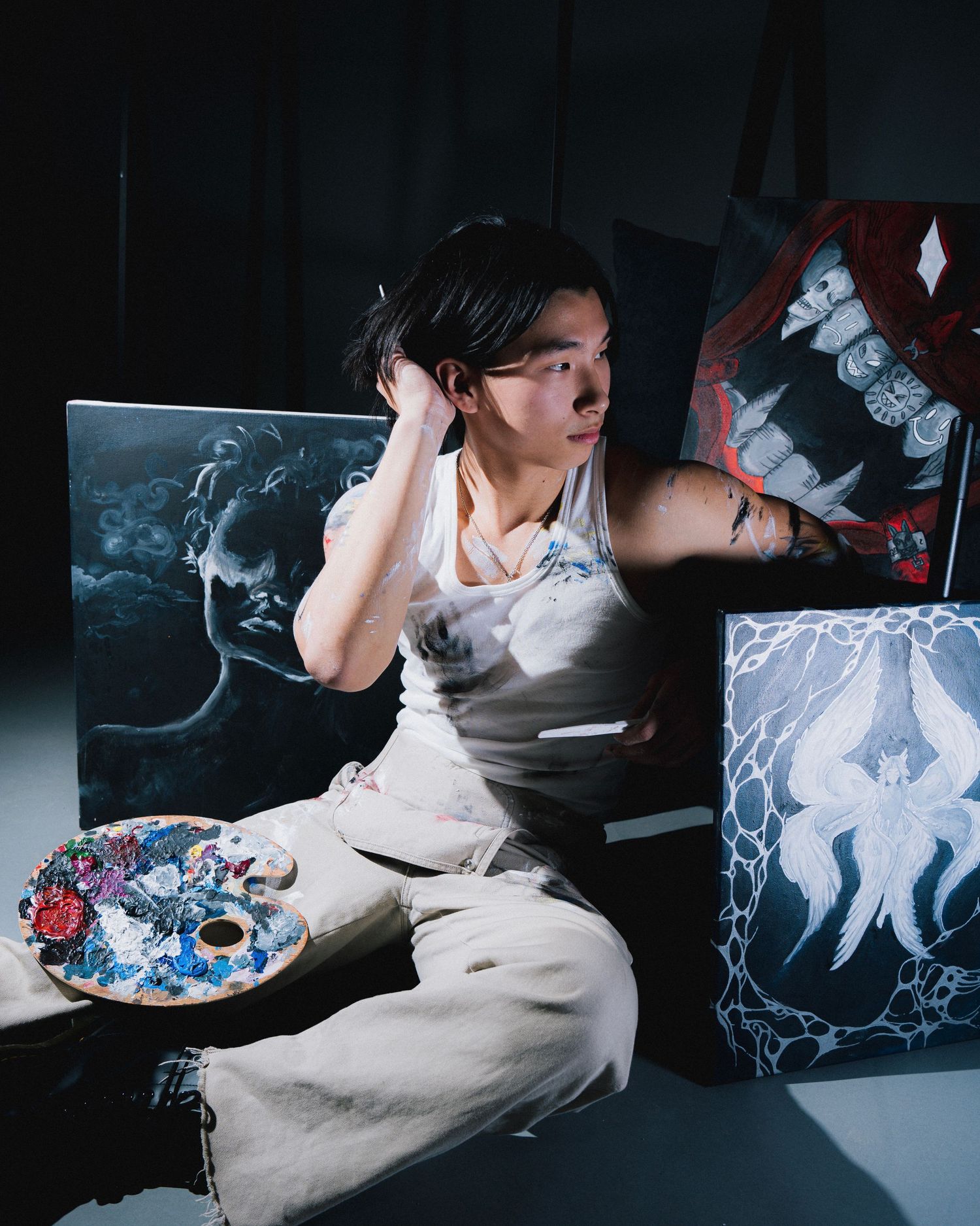Artist in white clothing surrounded by artwork and creative materials in studio setting.