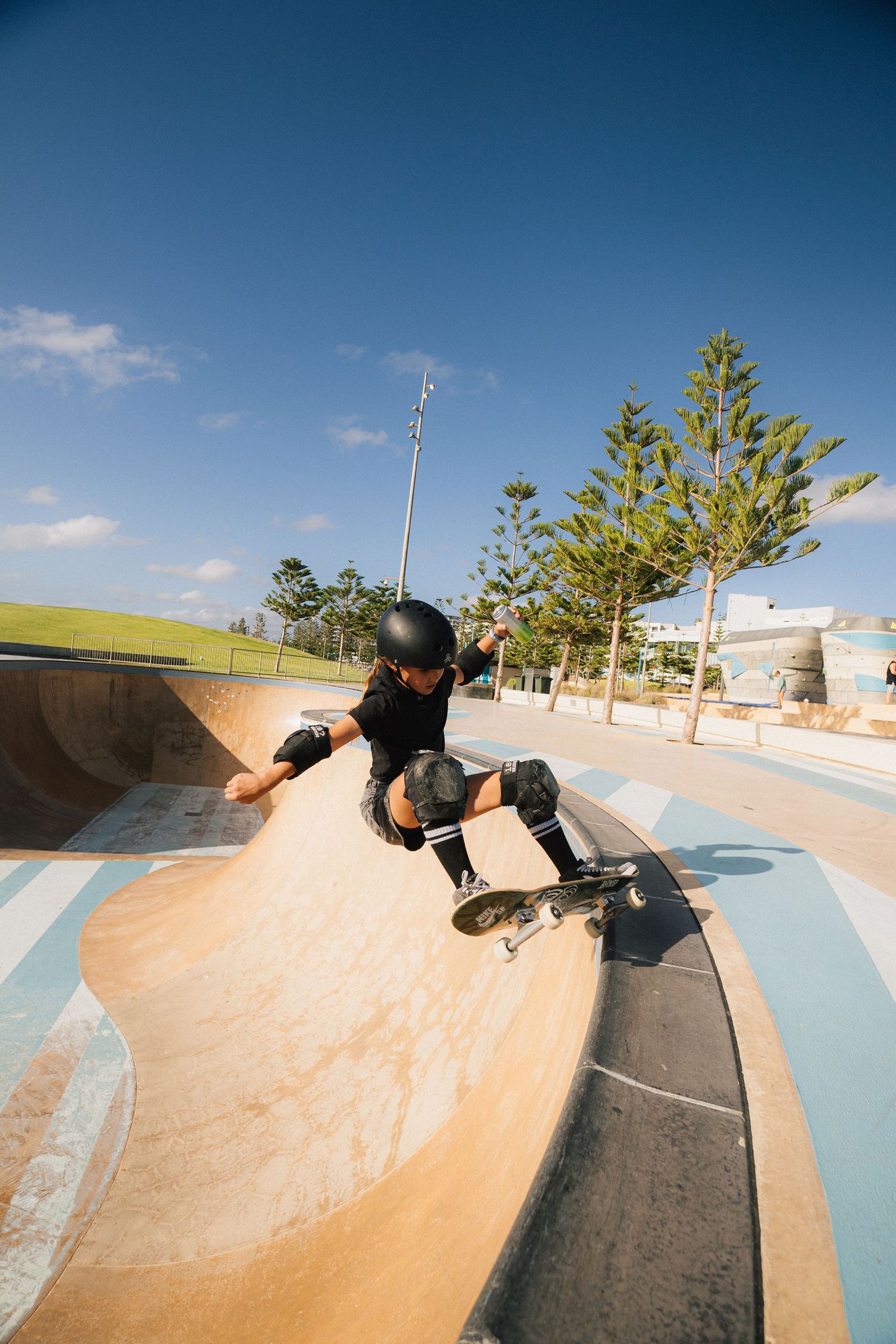 Skateboarder performs trick on concrete ramp at outdoor skate park under blue sky.