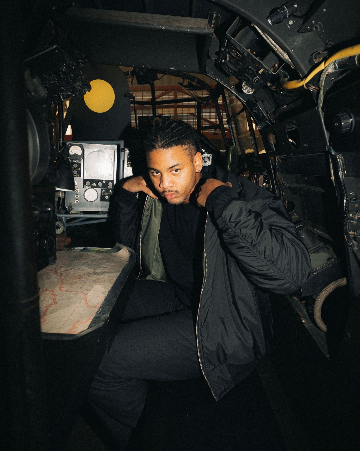 Person in black jacket poses inside dark vehicle interior with moody lighting and yellow moon visible through window.