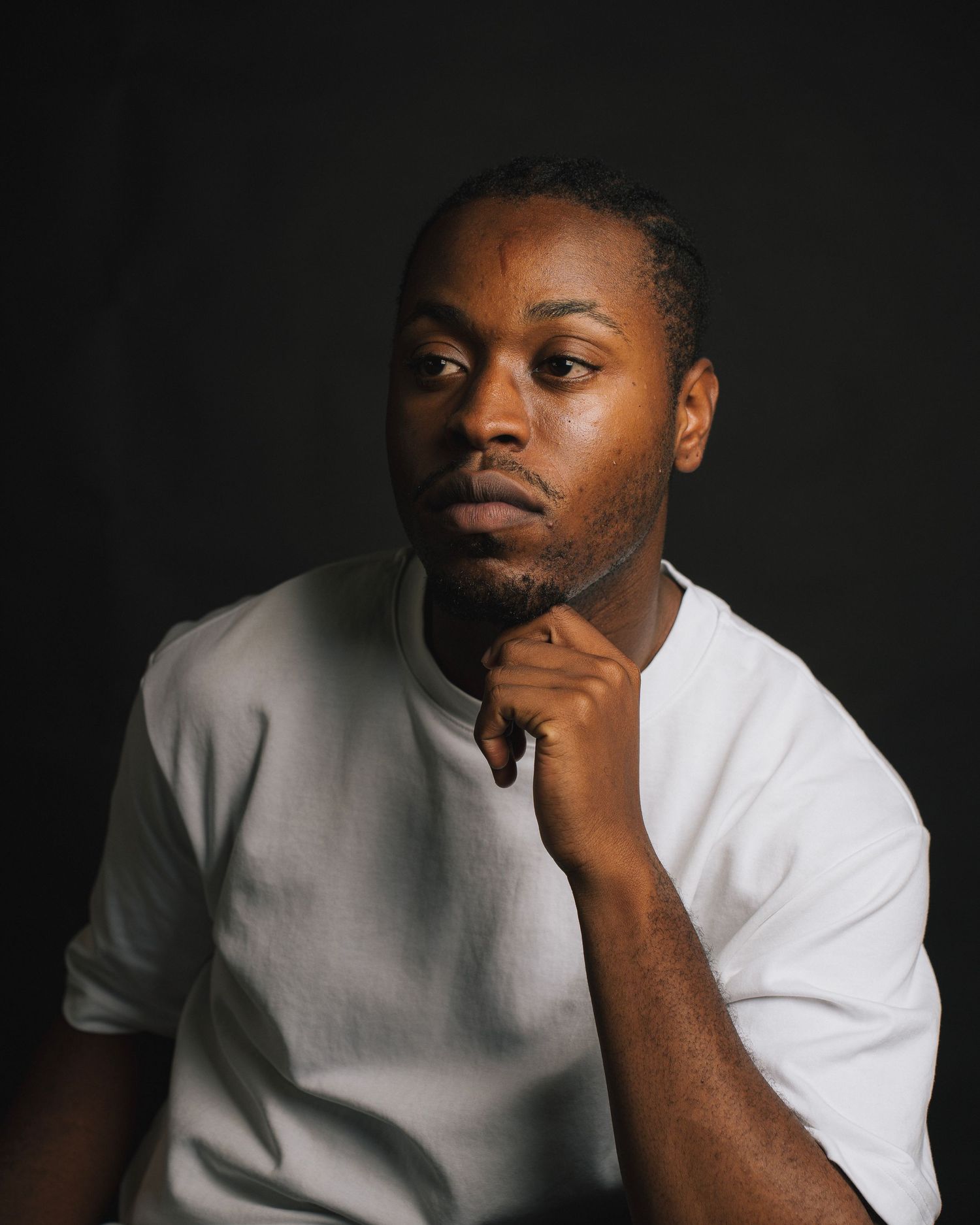Professional studio portrait of a person in a white shirt with thoughtful pose against dark background.