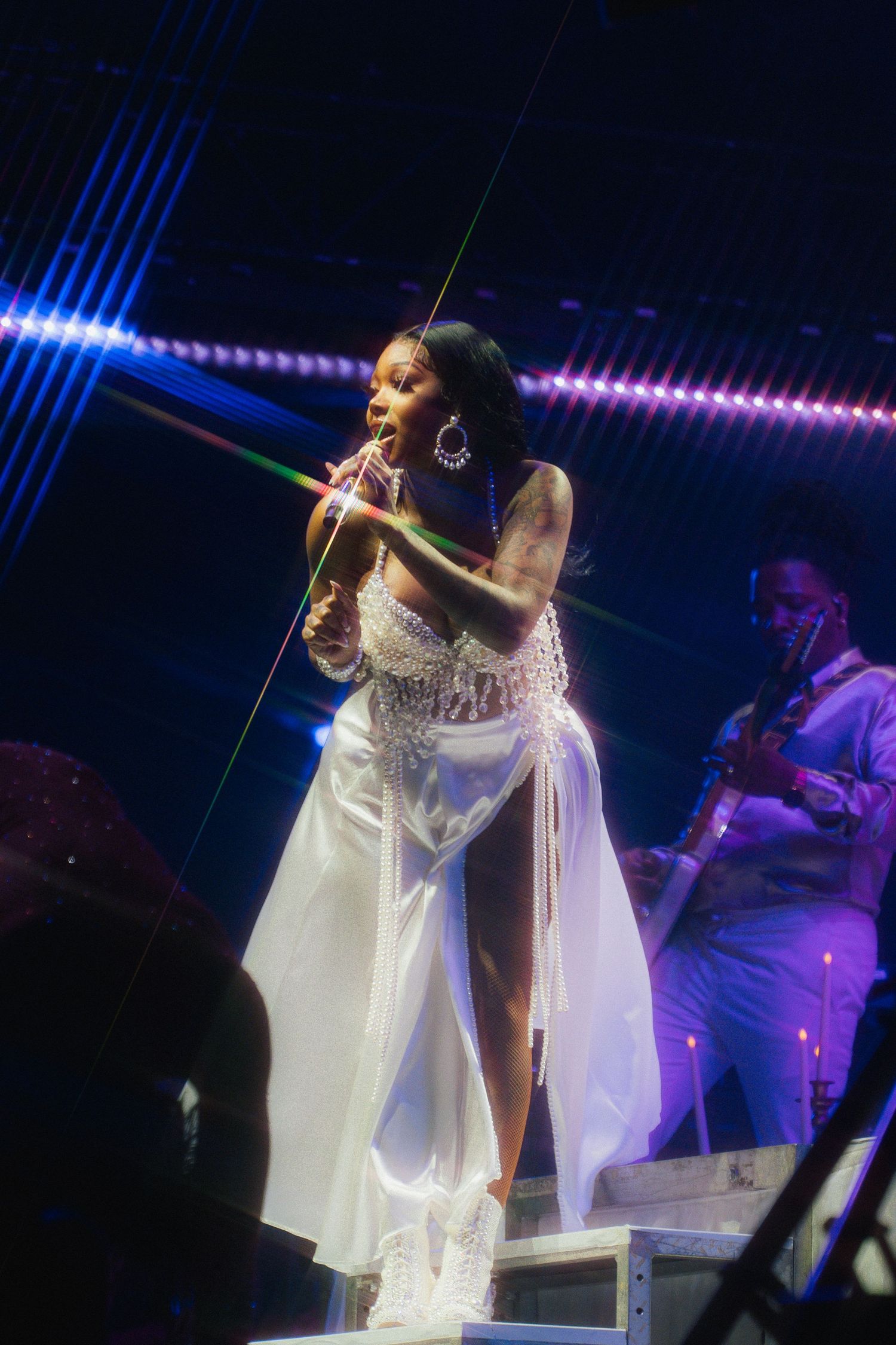 A performer in a flowing white dress sings passionately on stage with dramatic blue and purple lighting effects.