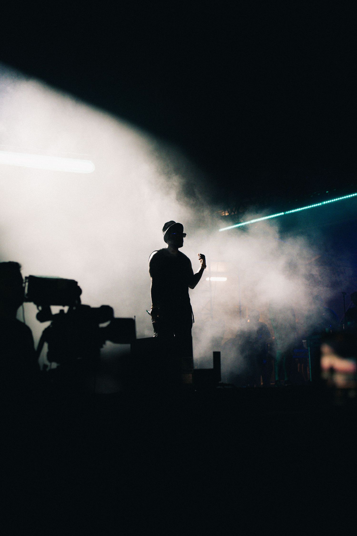 Silhouette of performer on stage surrounded by atmospheric smoke and dramatic blue laser beam lighting effects.