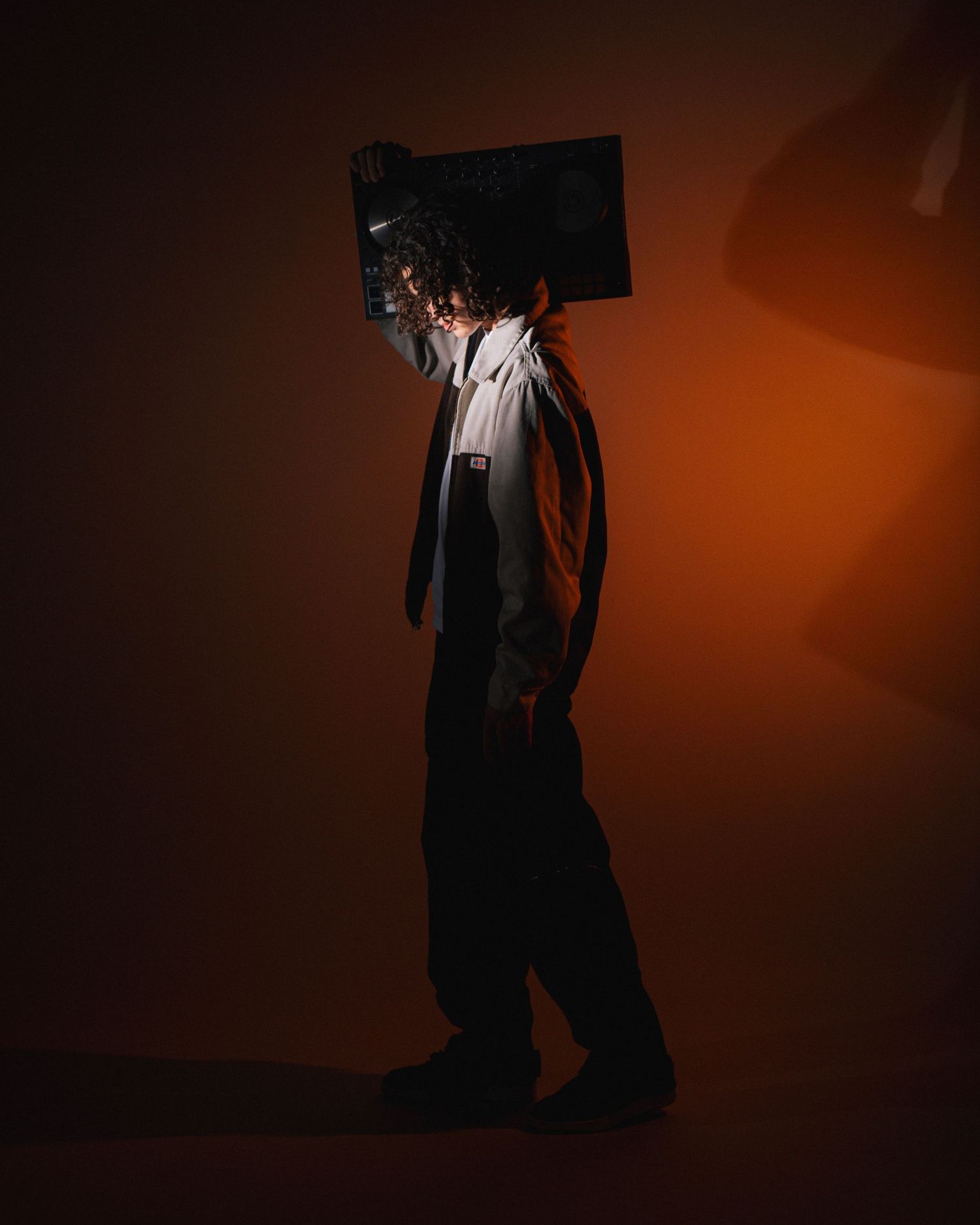 Black-clad figure walking in dramatic lighting against orange background with TV or monitor balanced on head.