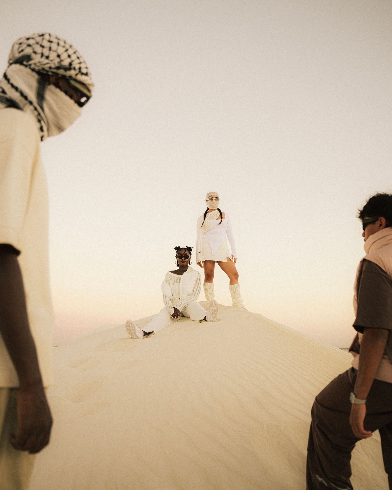 Group photoshoot on sand dunes with dramatic lighting and white outfits.