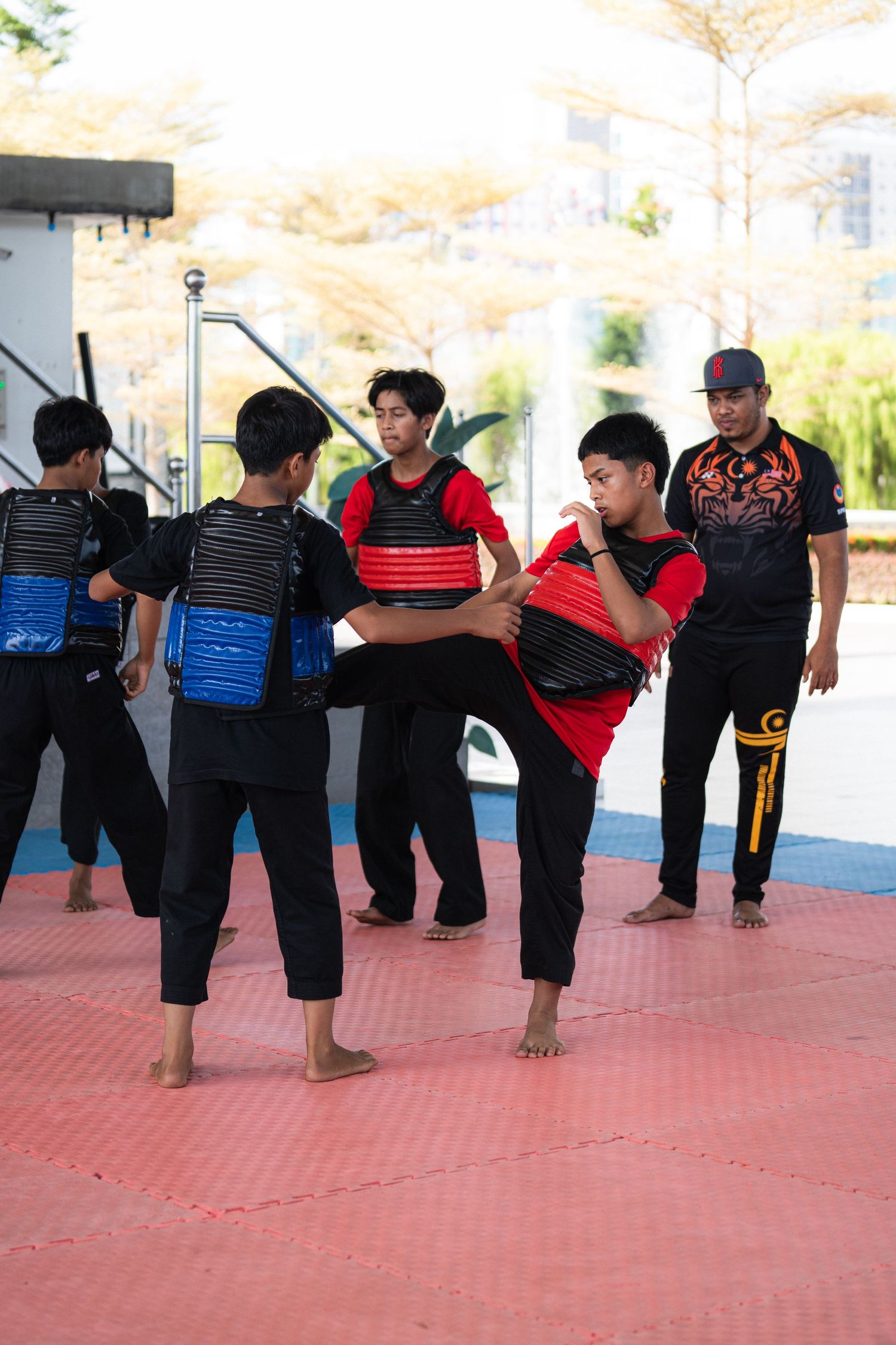 Martial artists in protective gear practicing moves on outdoor red mats.