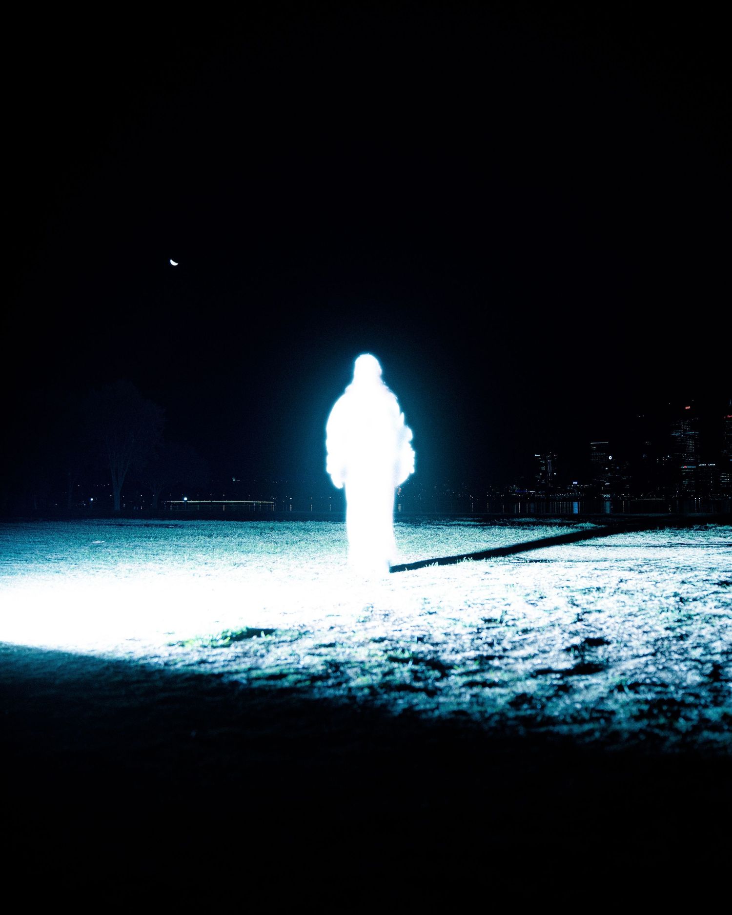Glowing silhouette figure standing in snowy landscape at night with ethereal blue light.