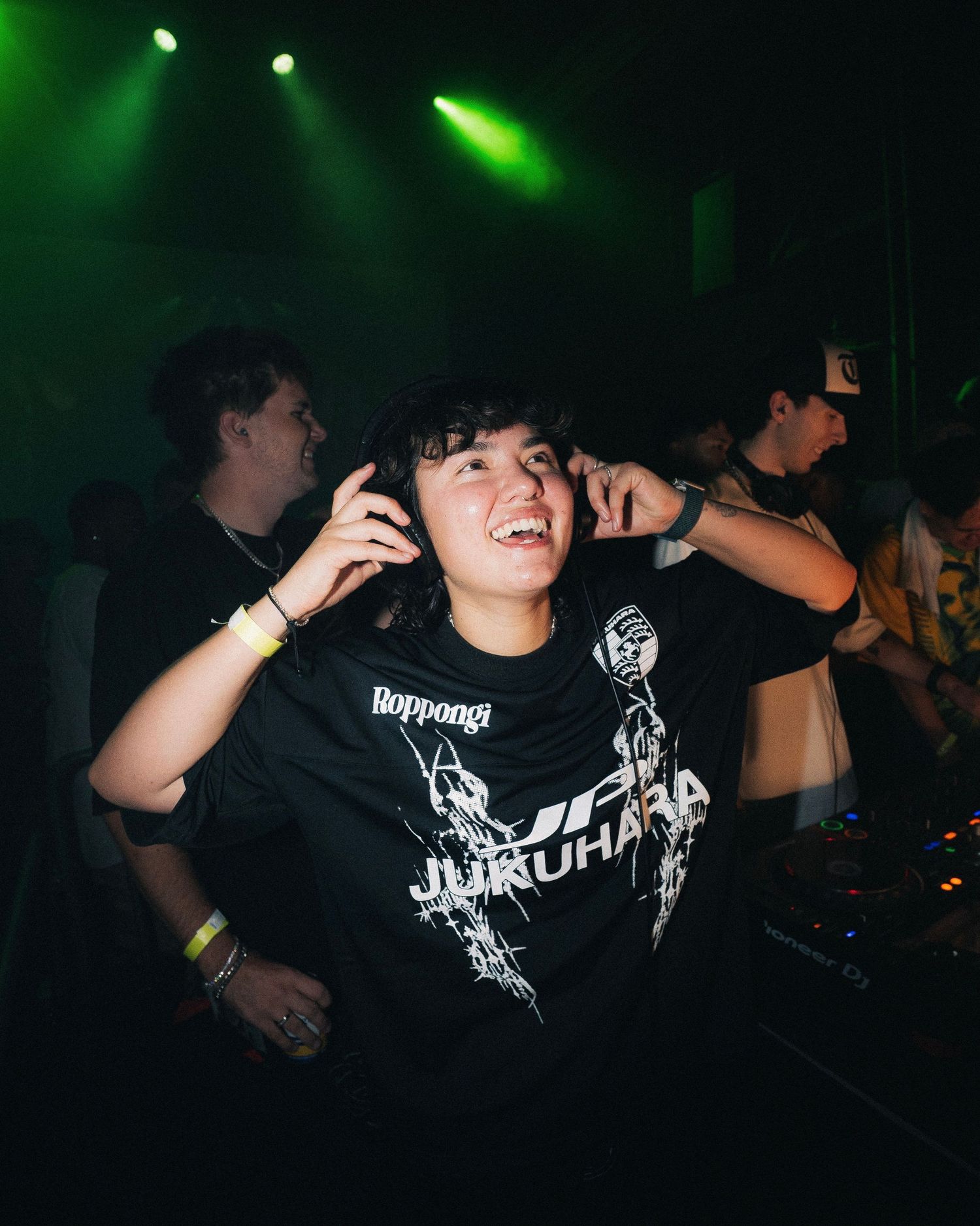 Concert attendee enjoying music with hands raised in a club under green lighting.