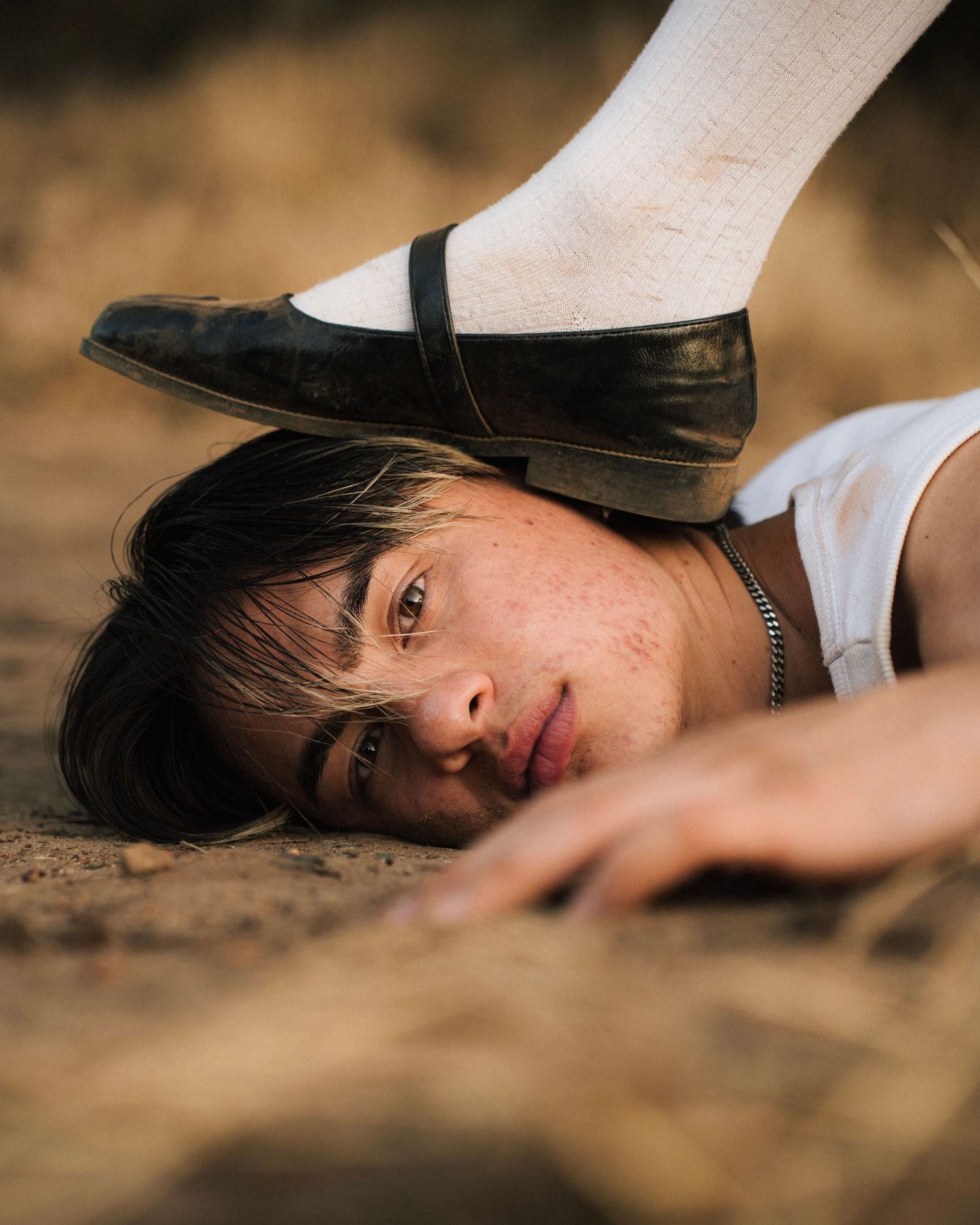 Creative portrait with a black dress shoe positioned over someone lying on sandy ground.