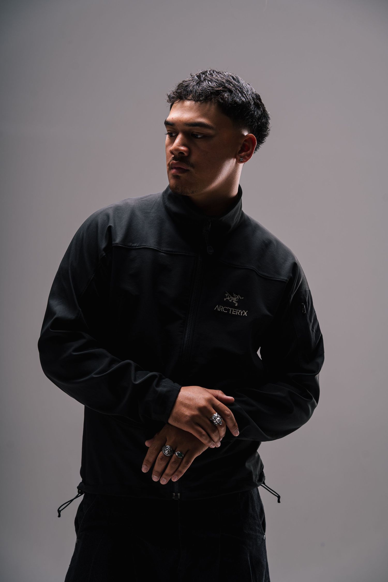 Stylish portrait of someone wearing a black Arc'teryx jacket against a gray backdrop with dramatic lighting.