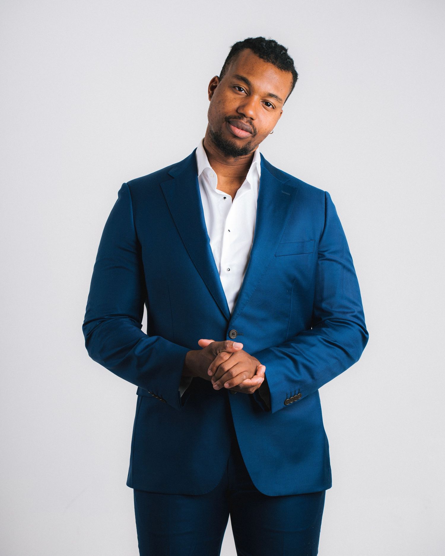 Person wearing a navy blue suit with white dress shirt stands confidently against light gray background.