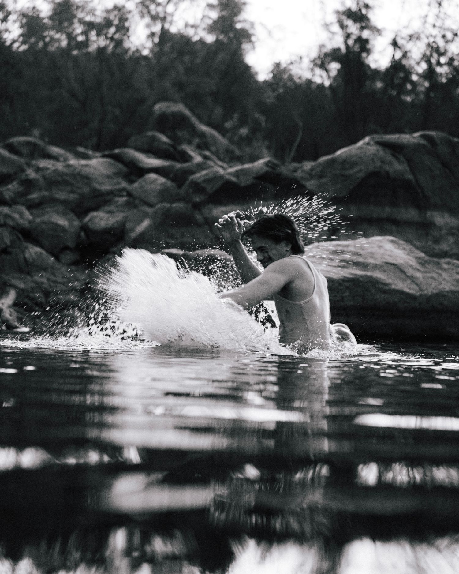 A dramatic black and white photograph captures water splashing in a natural swimming hole surrounded by rocky outcrops.
