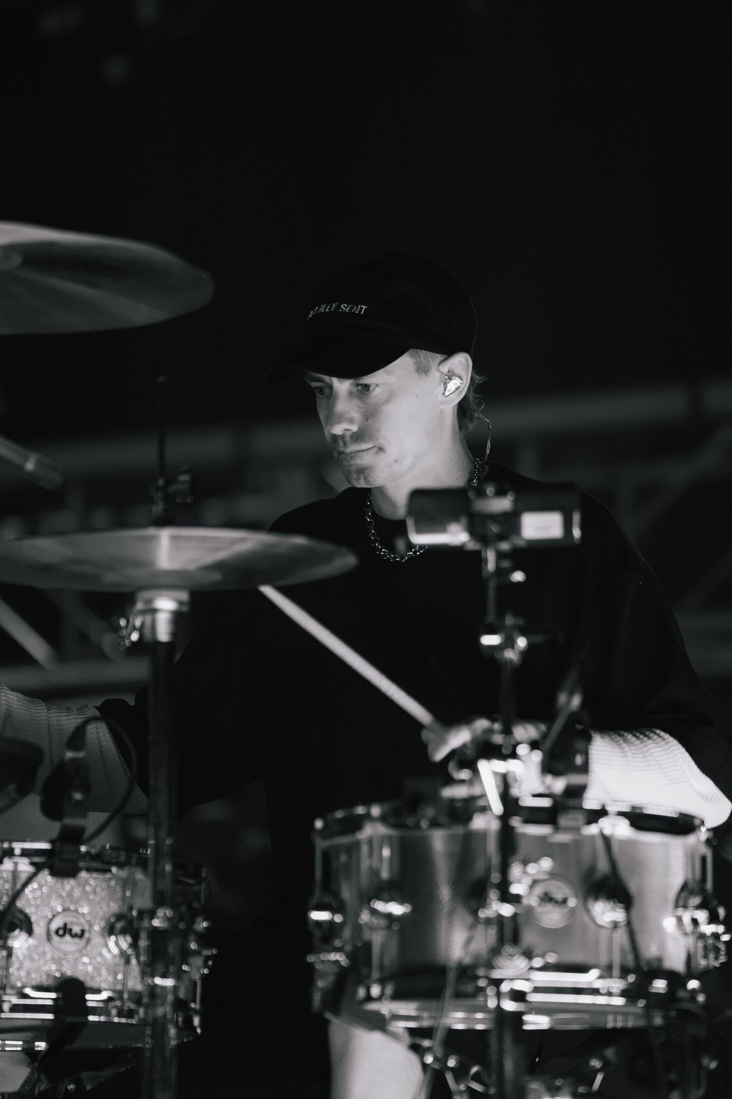A black and white photo of a drummer in a baseball cap behind a drum kit during a performance.