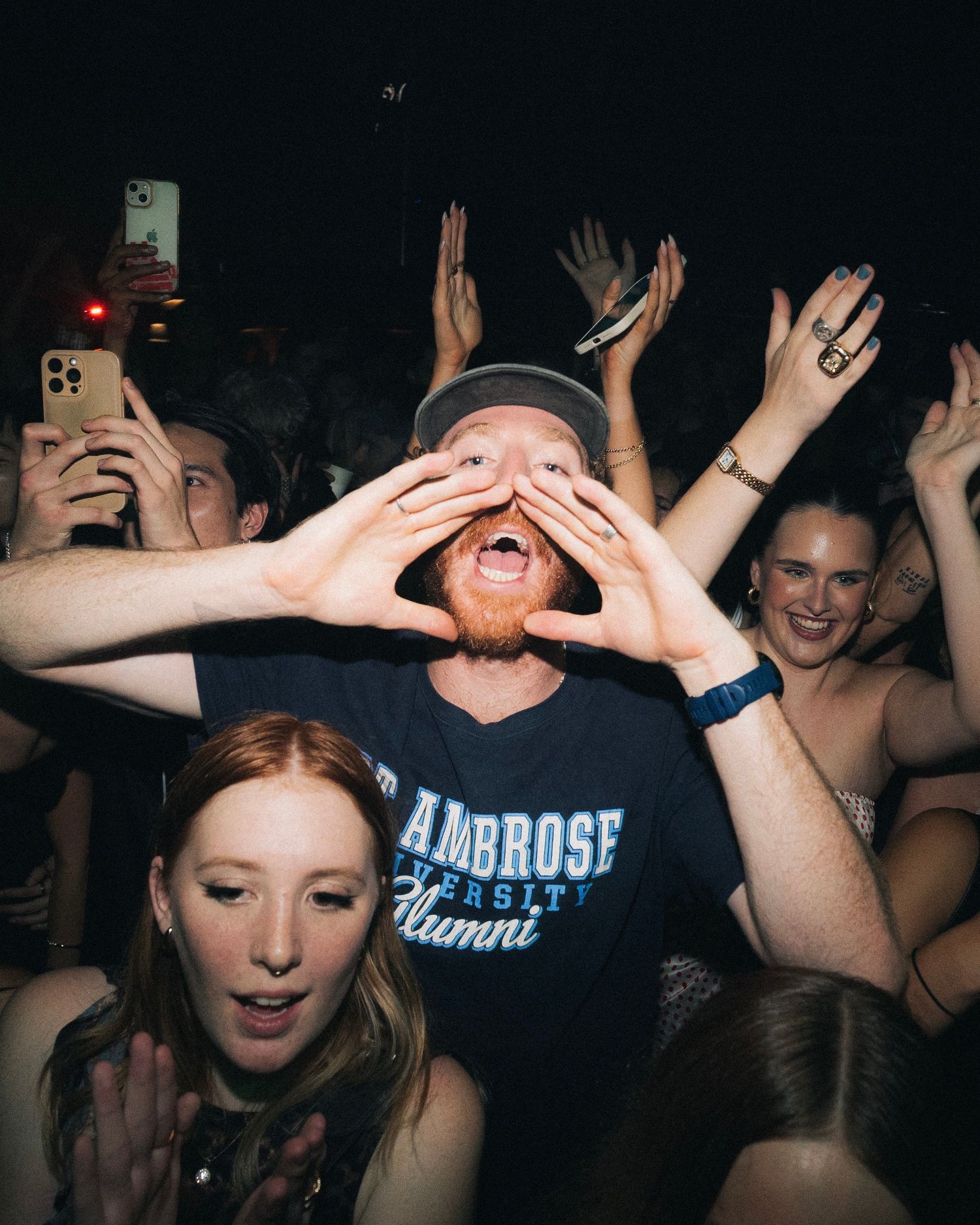 Enthusiastic concert crowd reacting with raised hands and expressions of joy at dark venue.