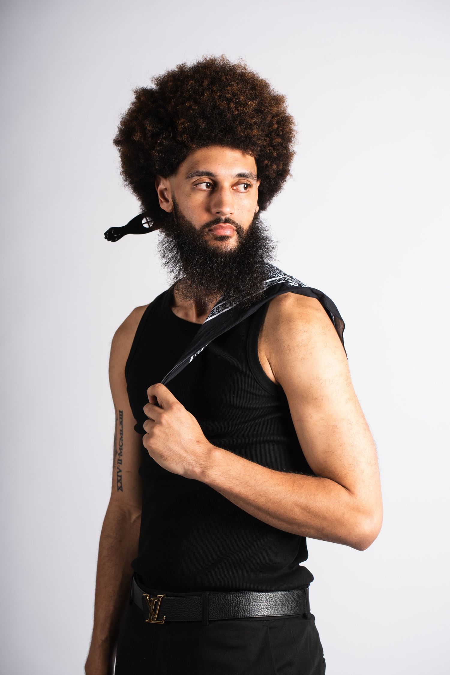 Athletic person with curly afro hairstyle wearing black tank top poses against light background.