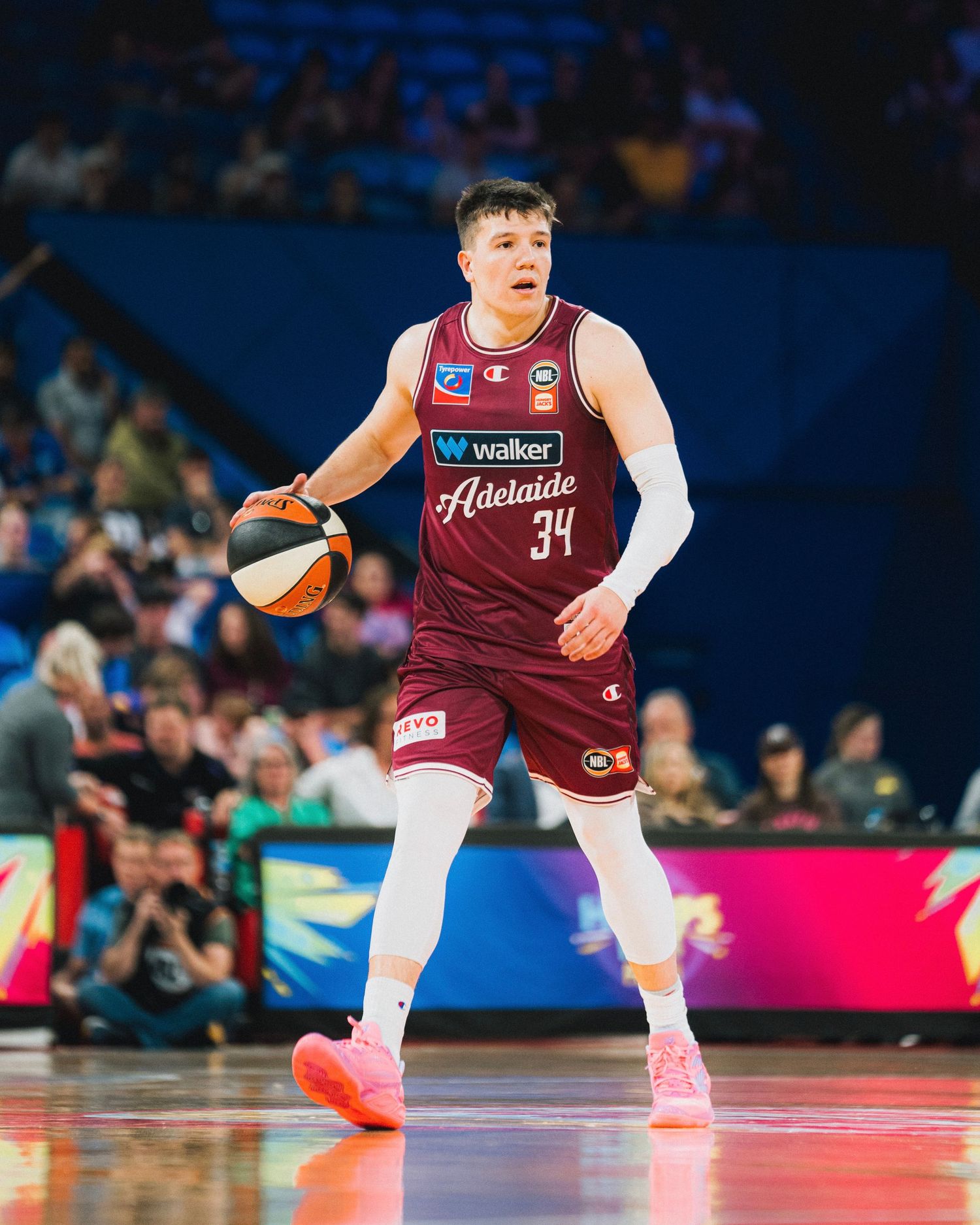 Basketball player in maroon Adelaide uniform dribbles ball during game.