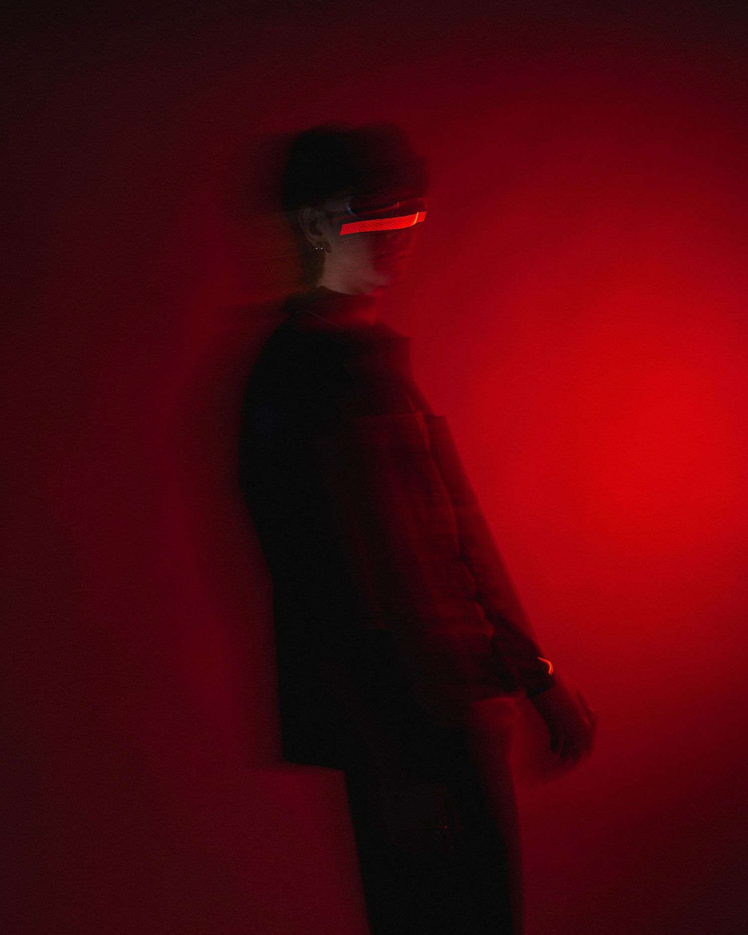 Silhouetted figure stands in profile against dramatic red lighting and dark background.