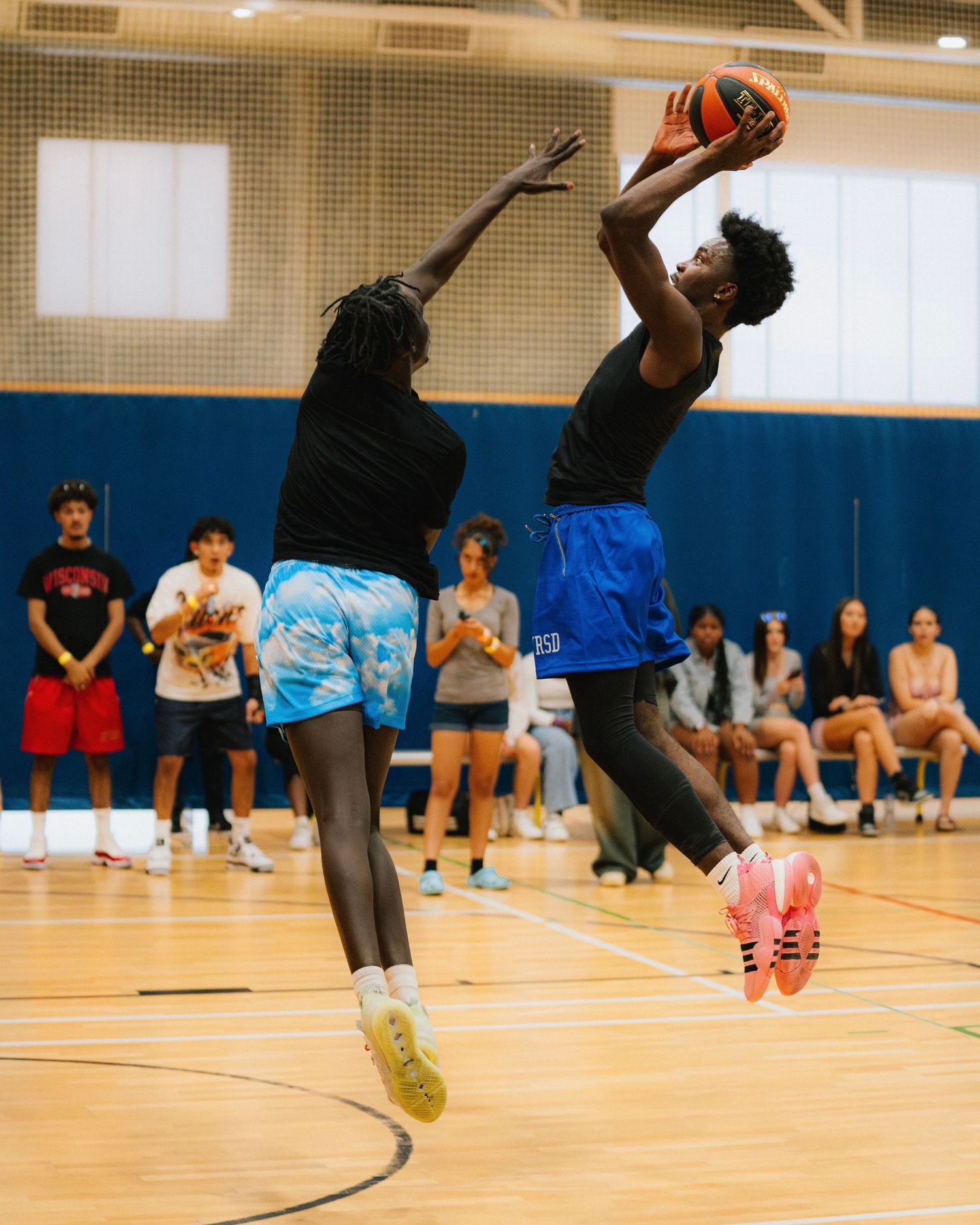 Two players jump high during a basketball game in an indoor gymnasium.