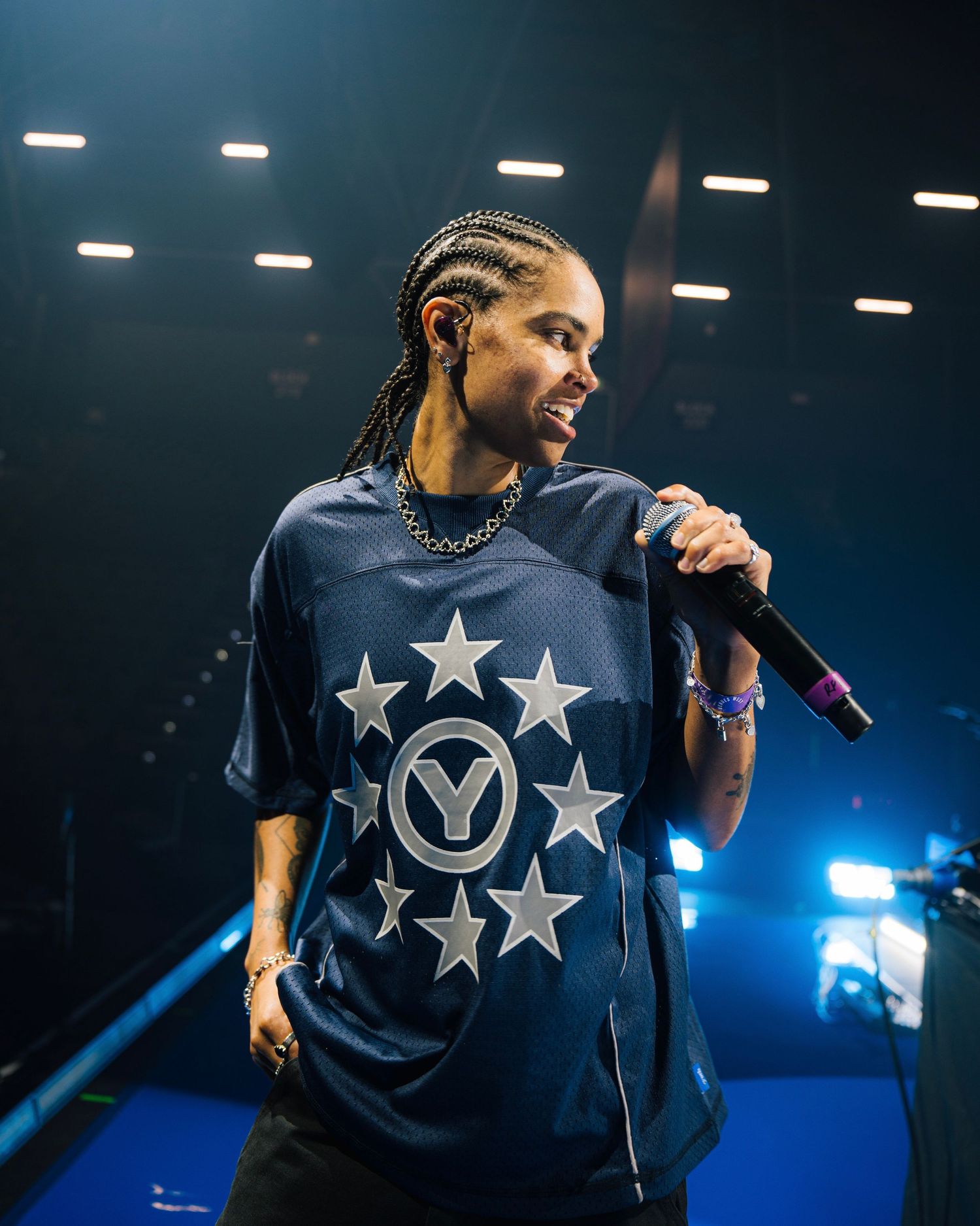 Artist performing on stage wearing navy t-shirt with star design and chain necklace under stage lights.
