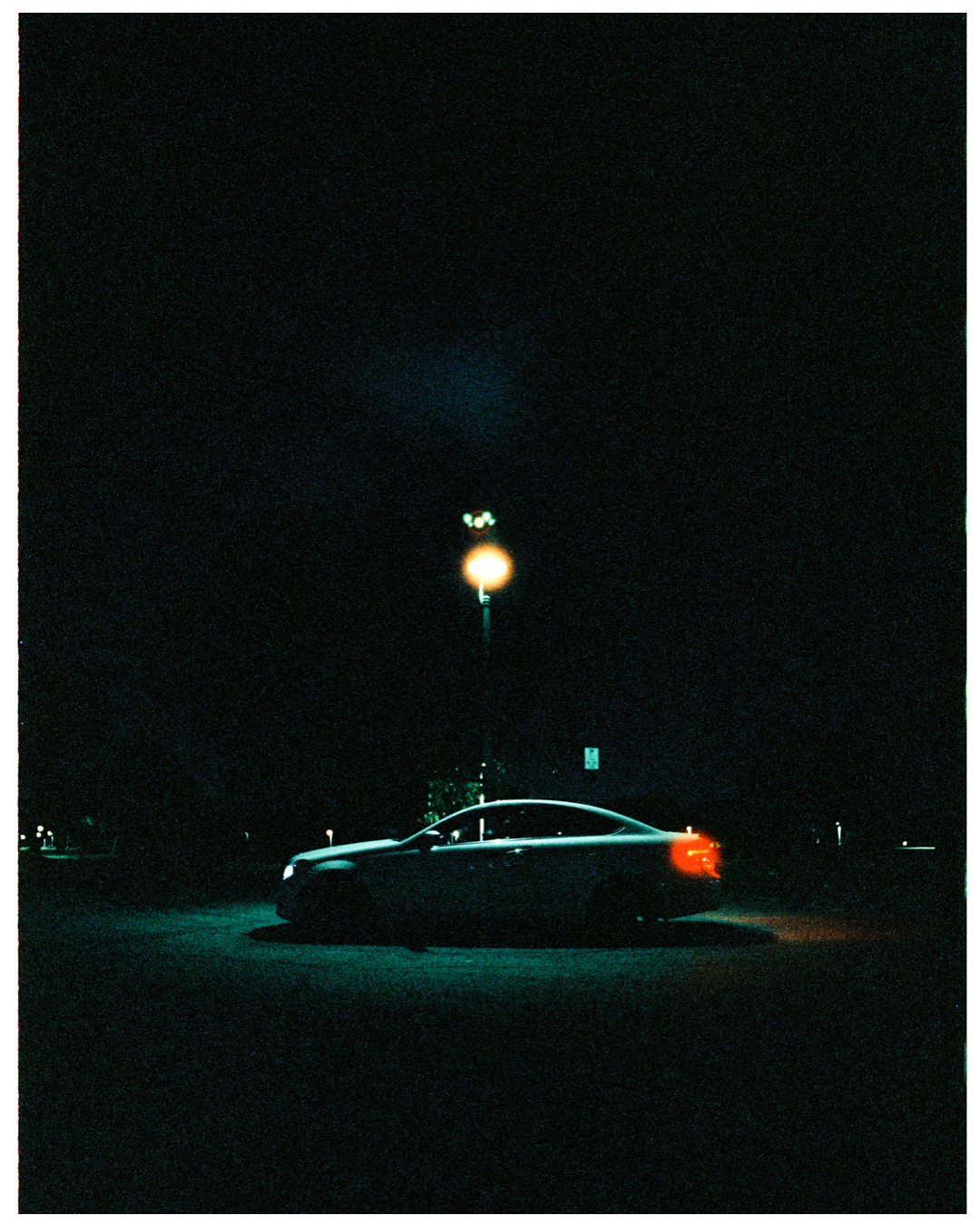 A dark car sits under a glowing street lamp at night, creating a moody urban scene with blue and red lighting.