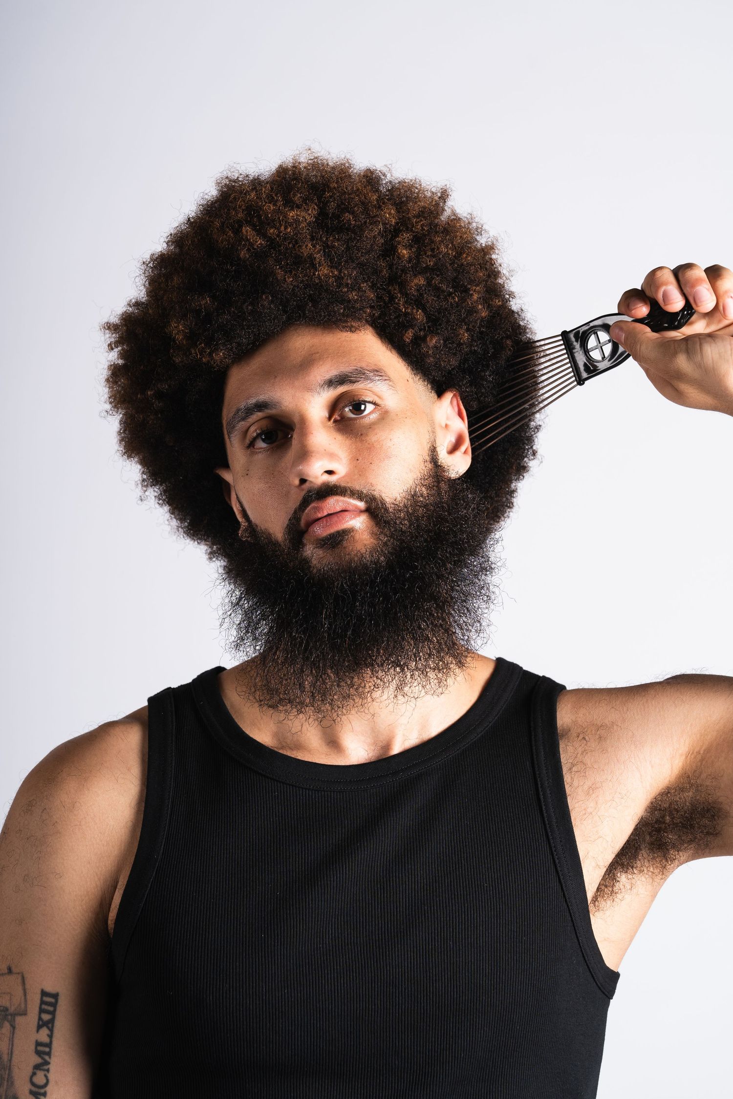 Four frames showing a person with natural curly hair and beard wearing a black tank top against a white background.