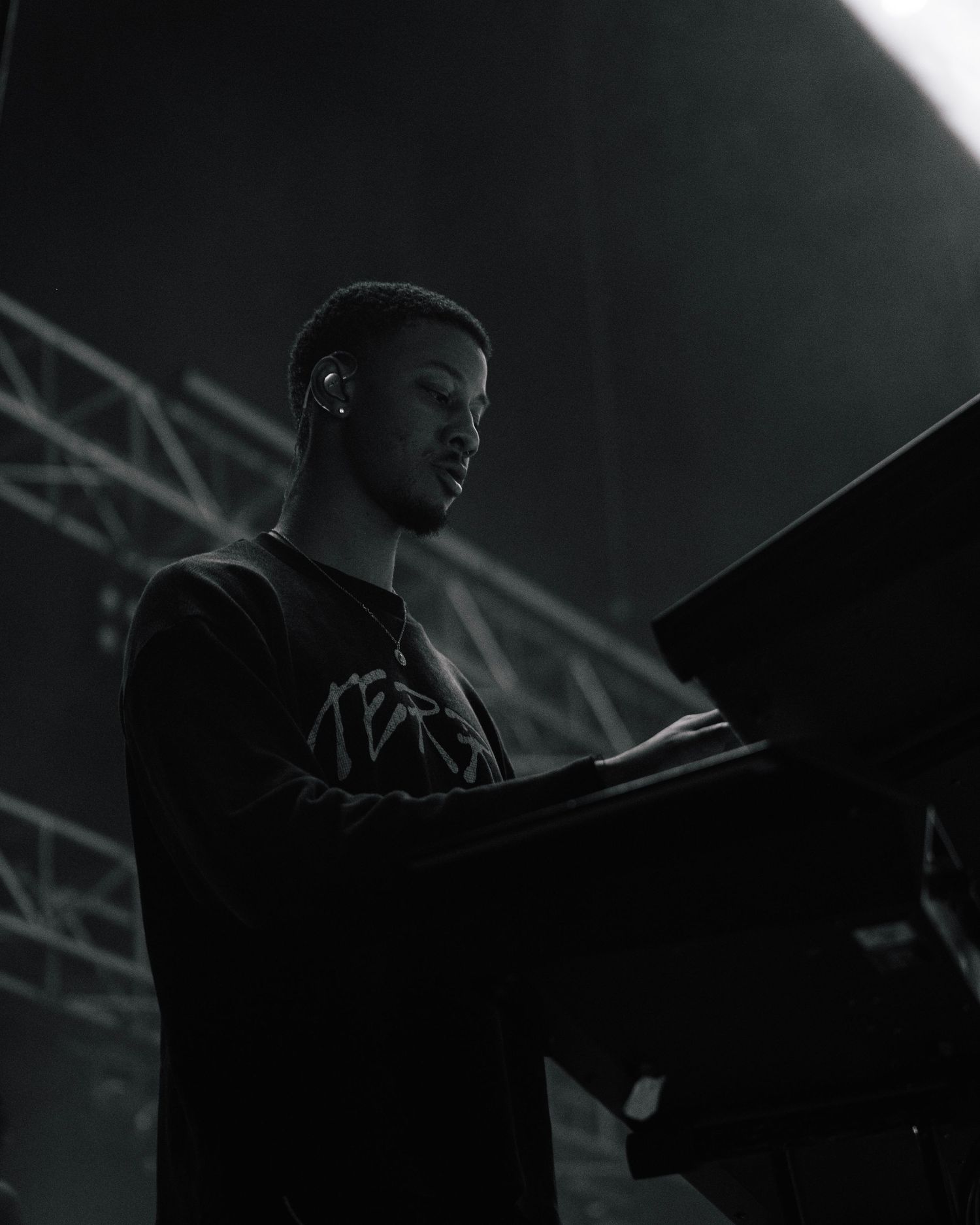 A person performs on stage in dramatic black and white lighting behind equipment during a concert performance.