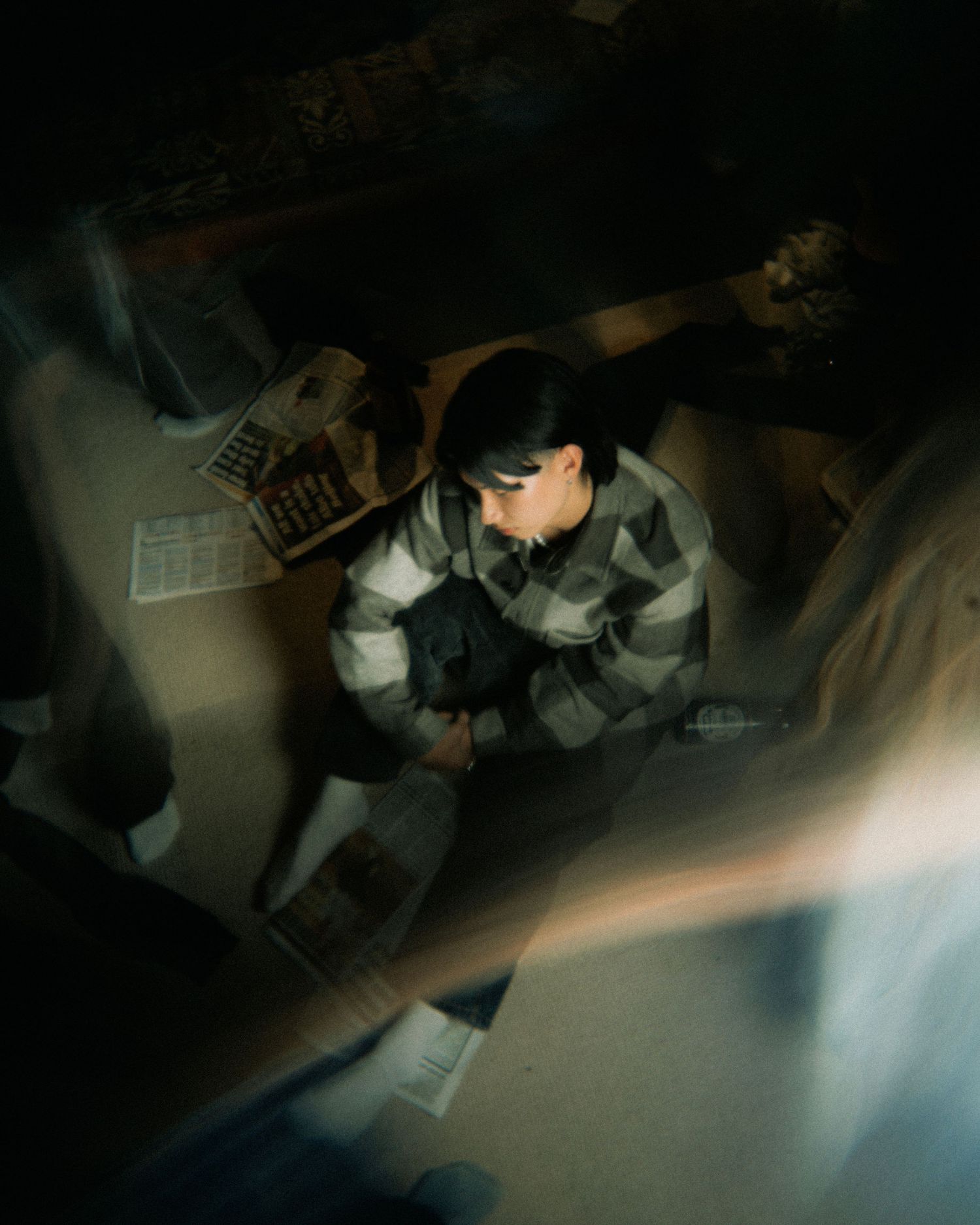 An aerial view showing someone sitting in a dark room with papers and documents scattered on the ground.