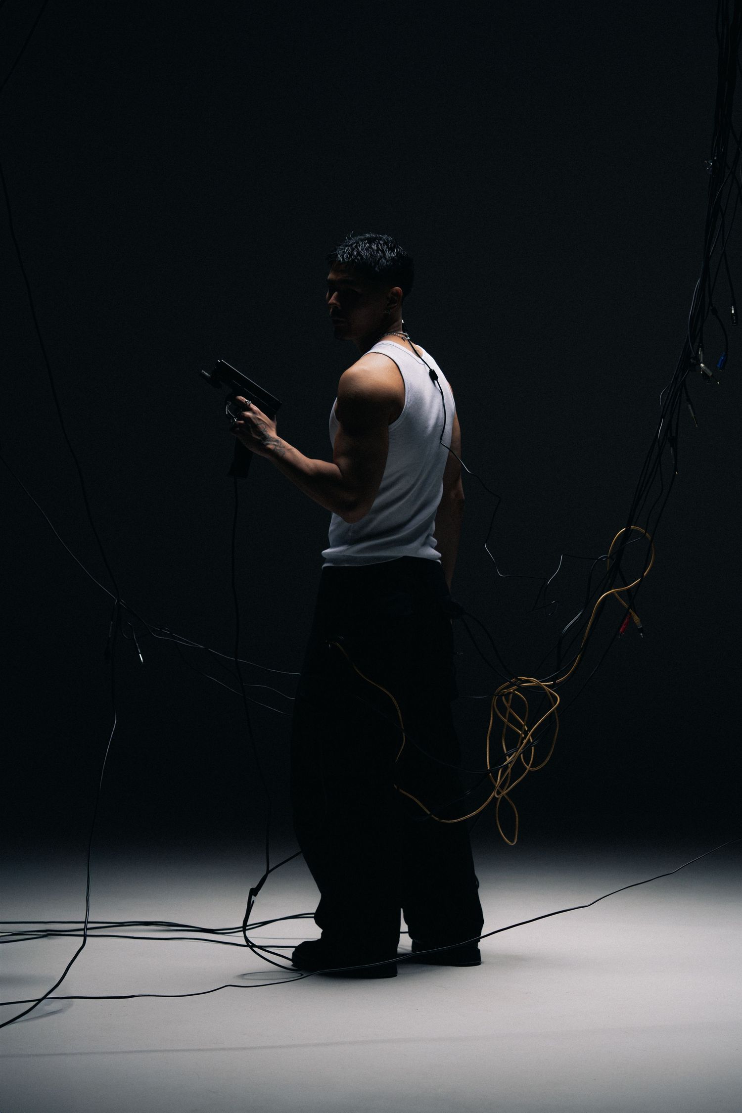 Dramatic silhouette of someone in a tank top standing among tangled cables in dark moody lighting against black background.