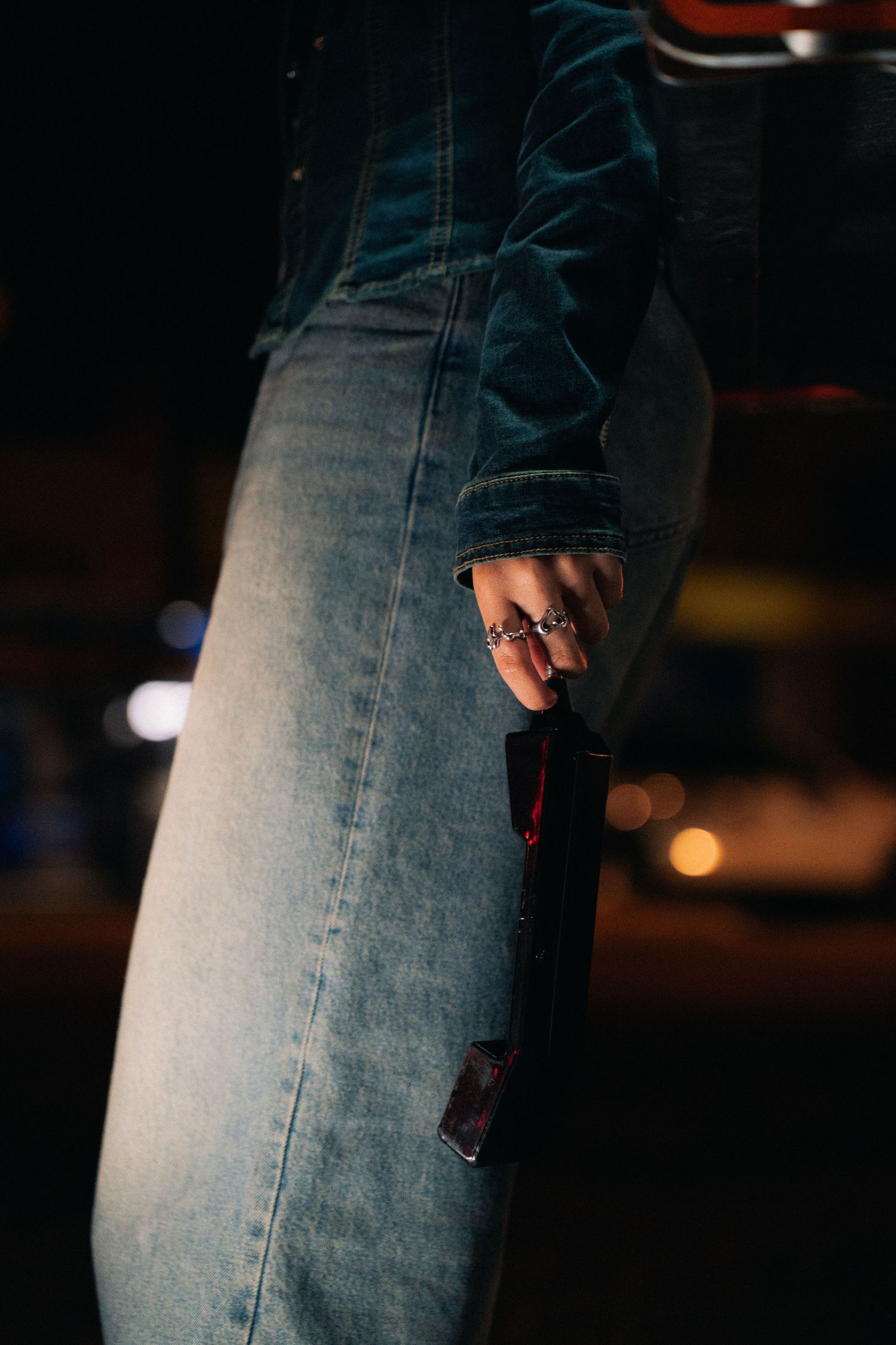 A close-up of worn blue jeans with ripped holes revealing skin underneath in dark lighting conditions.