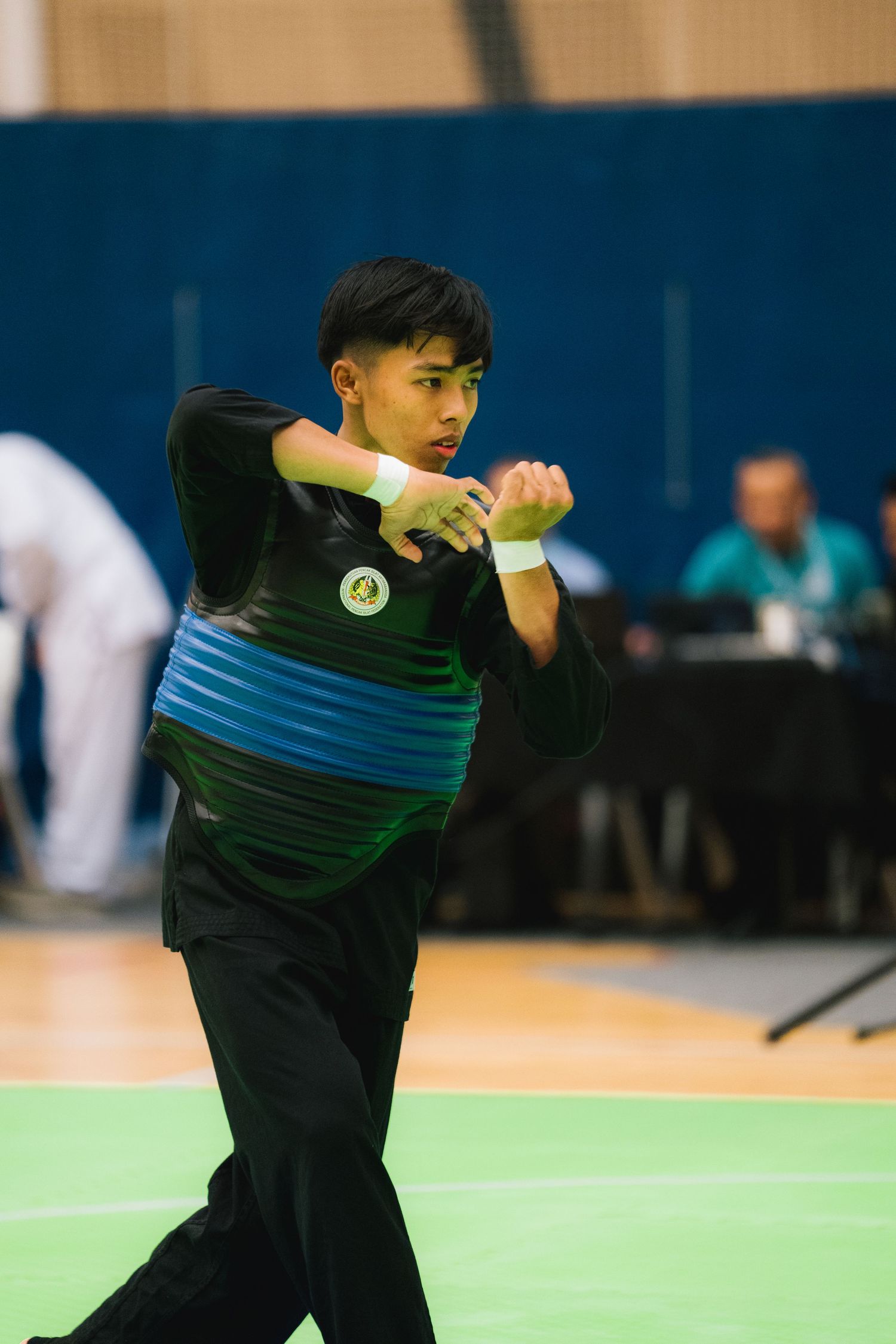 Athlete in black and blue uniform performs a martial arts routine during indoor competition.