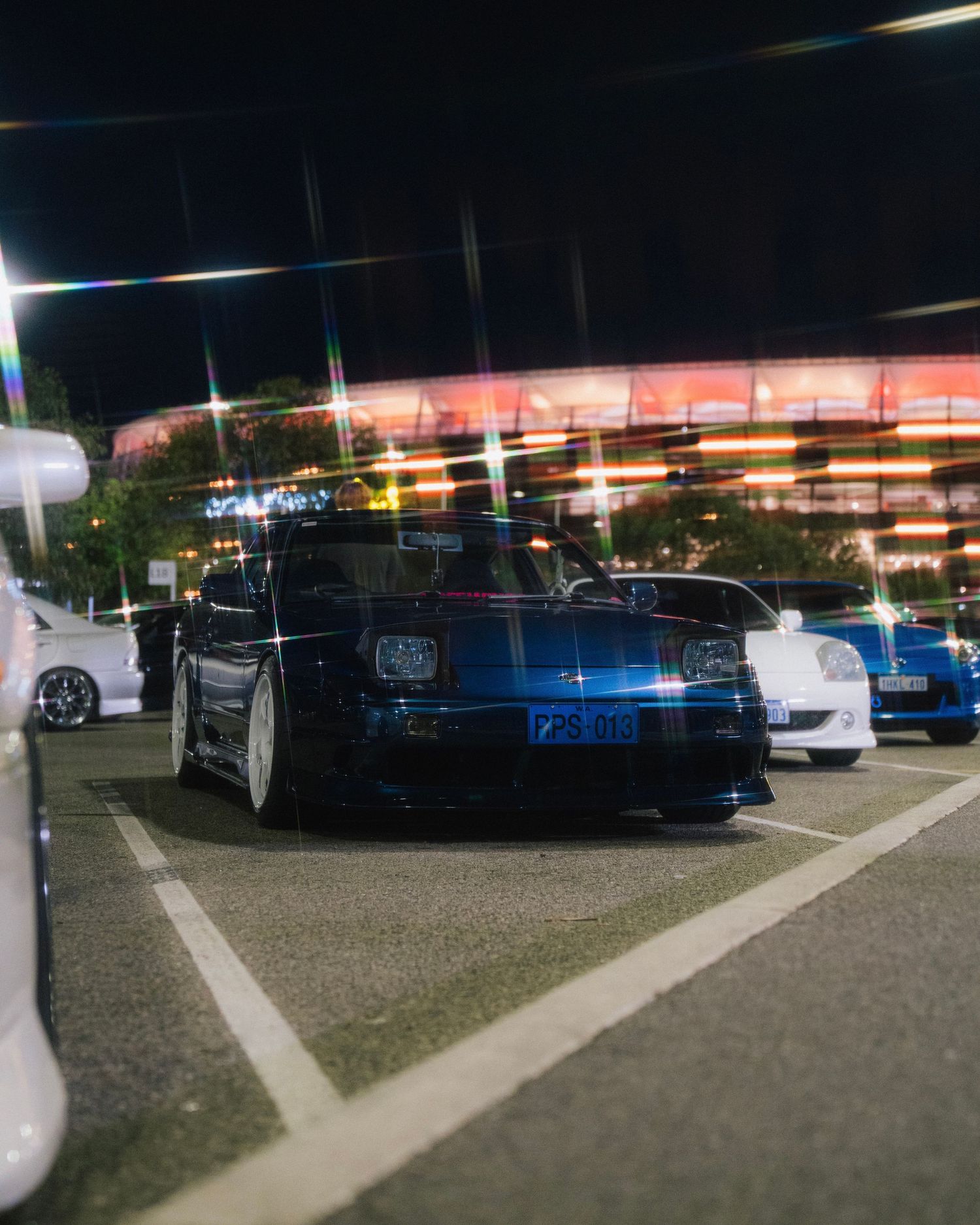 Dark blue modified Nissan sports car parked at night in a well-lit outdoor lot.
