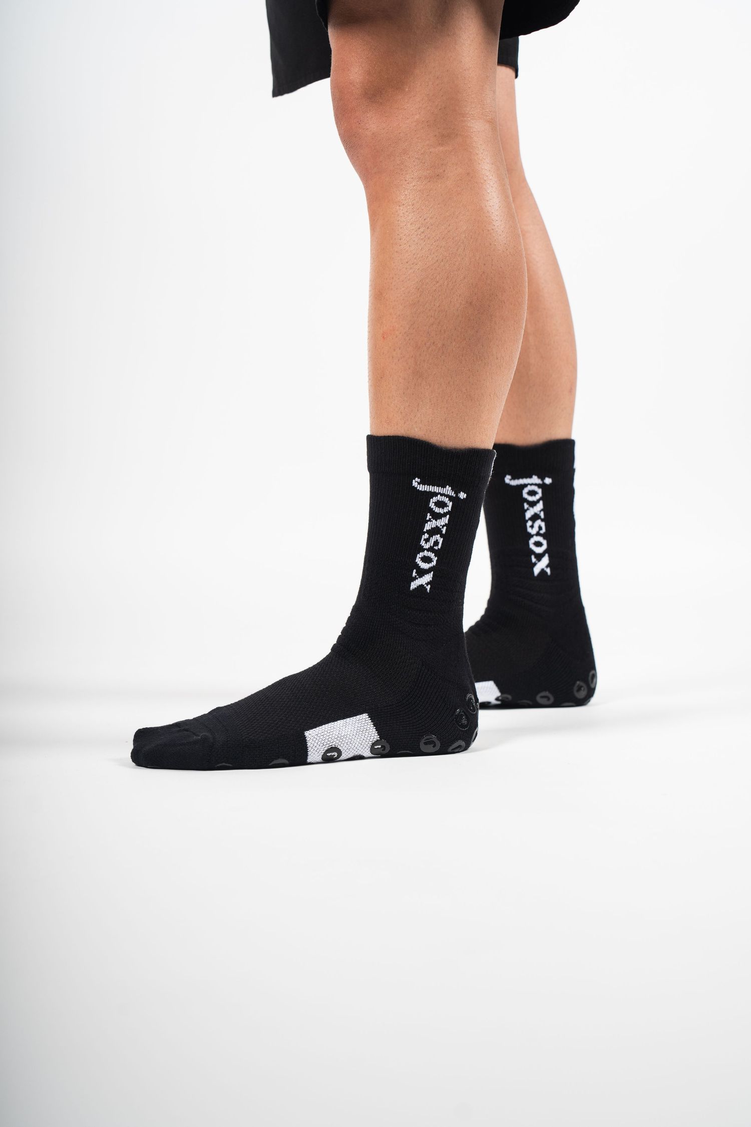 Side view of legs wearing black socks with white XOXO text design against white background.