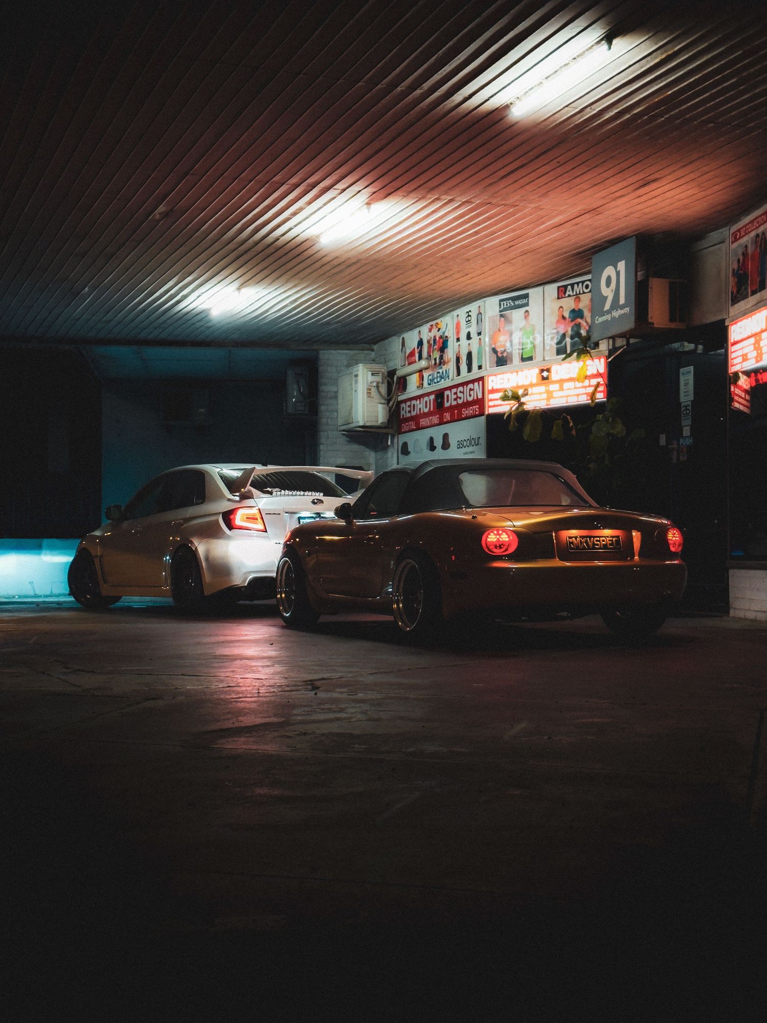 Row of modified Japanese sports cars parked against orange brick building facade.