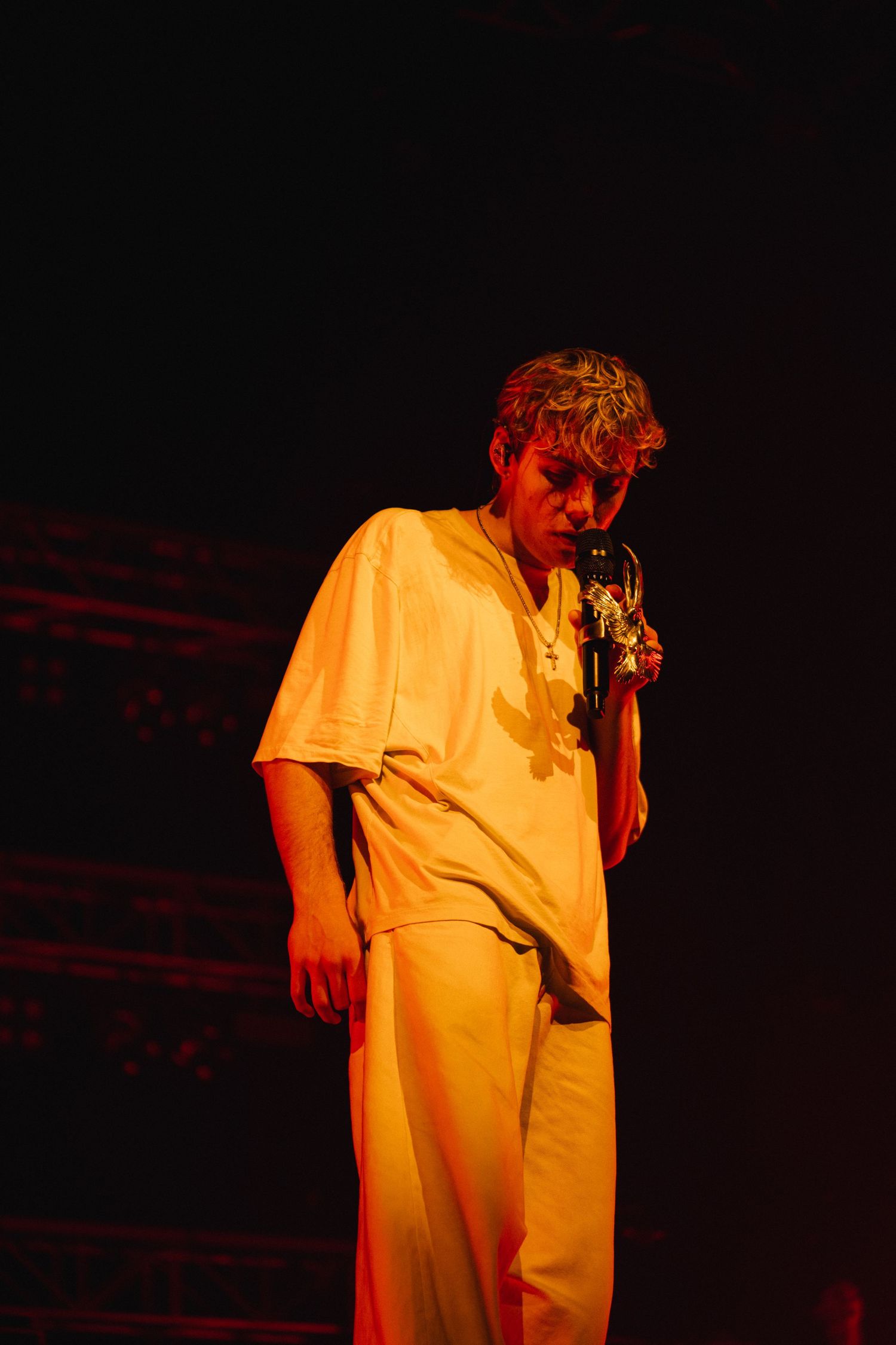 A performer in an all-yellow outfit stands on stage under dramatic red lighting during a show.