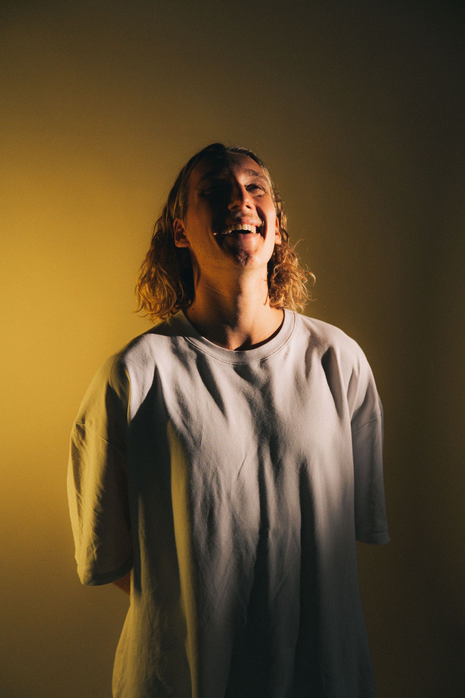 A series of moody portraits showing someone in a white t-shirt against a golden wall with dramatic shadows.