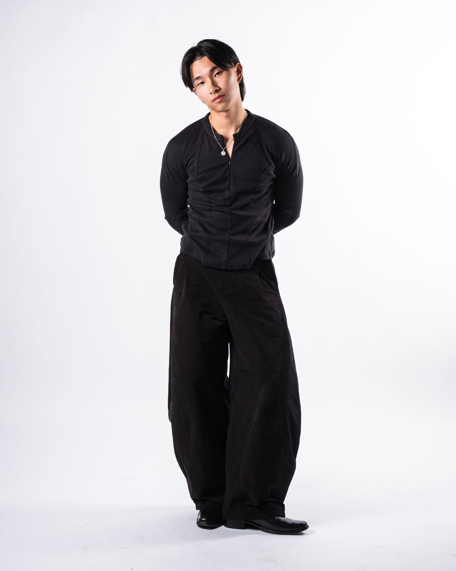Figure in a black outfit poses against white background showing different angles and stances in a candid photo series.