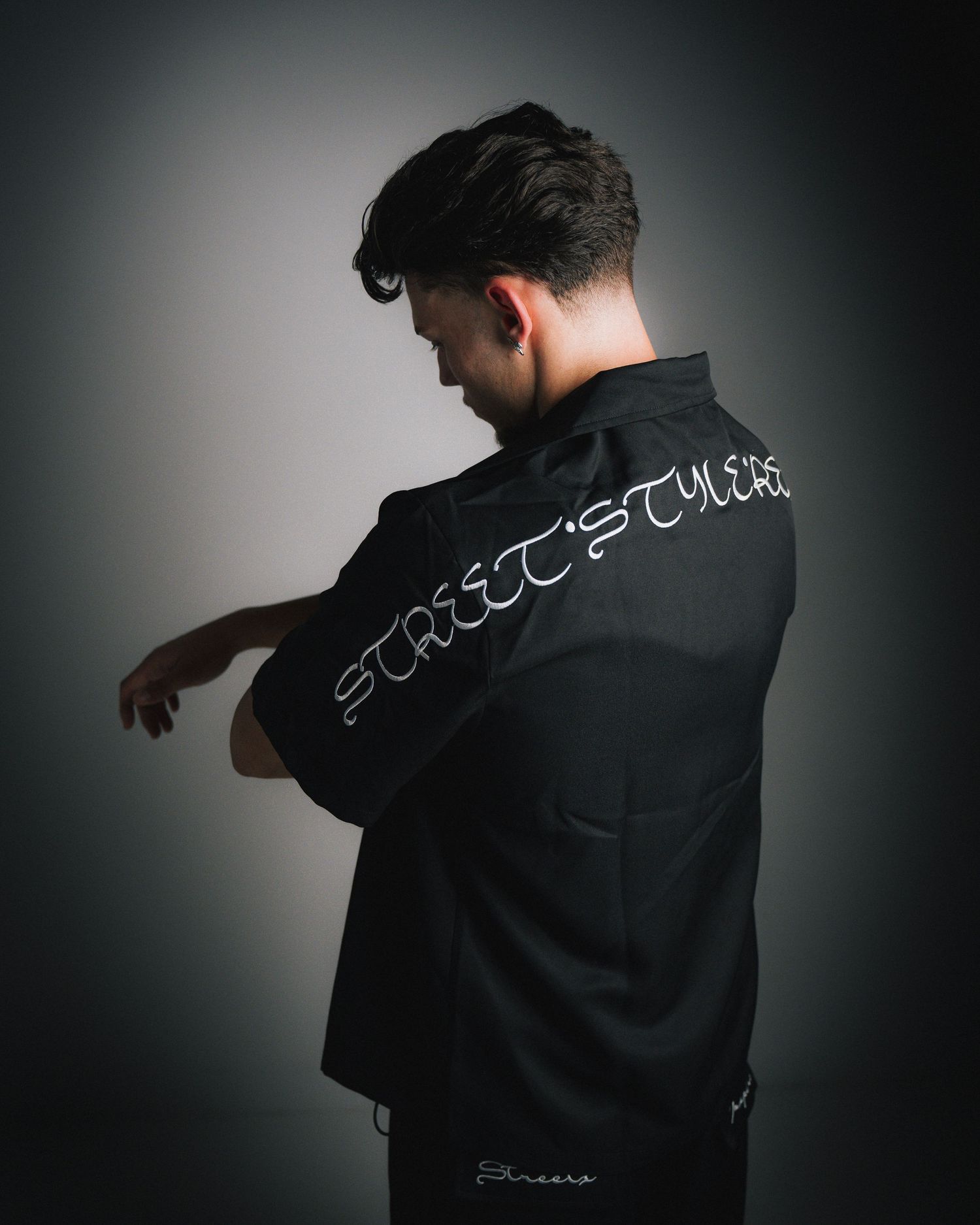 Side profile of person wearing black jacket with text design in dramatic lighting.