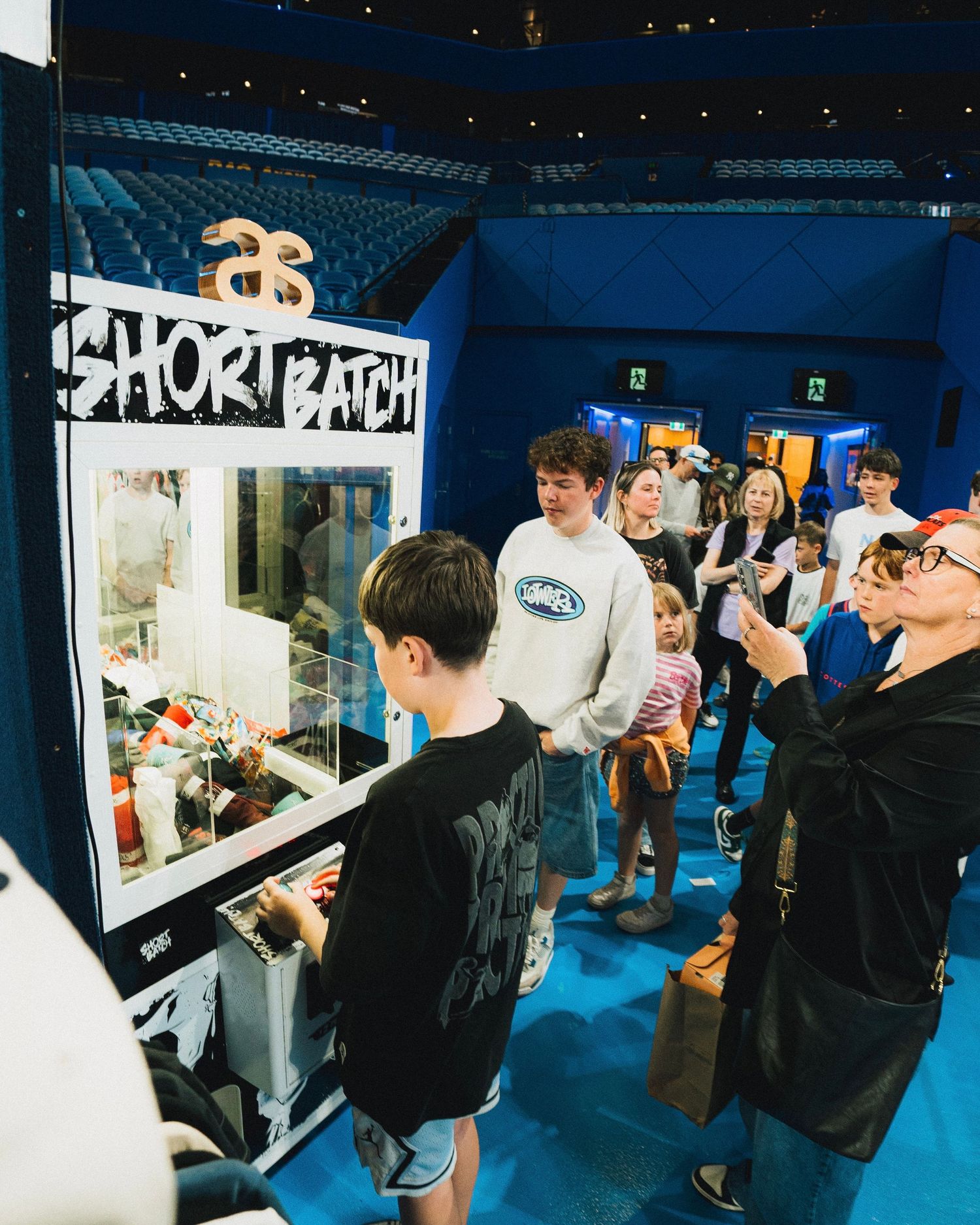 People lined up at an arcade claw machine game display with glowing blue lighting.