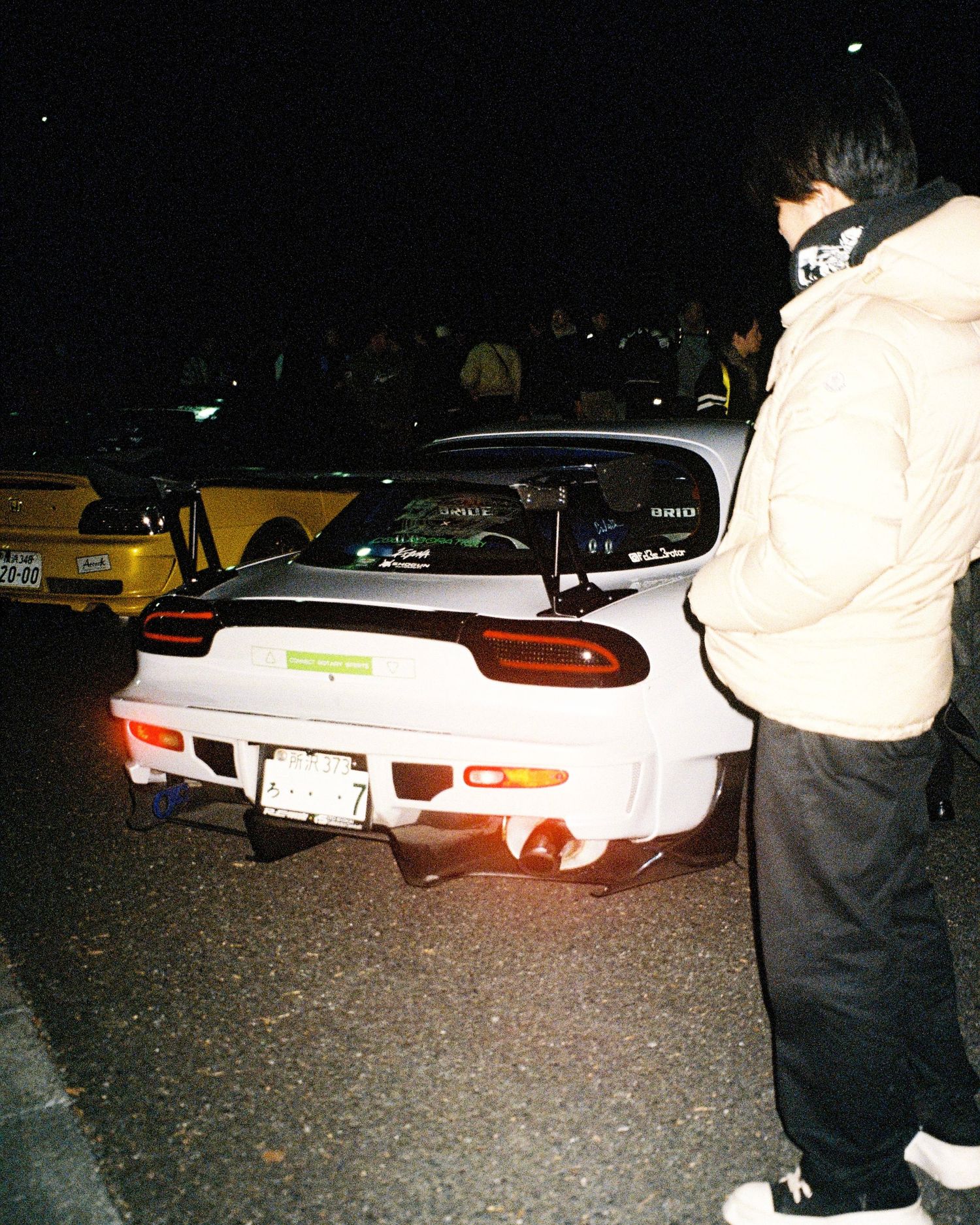White modified Mazda RX-7 rear view showing custom taillights and spoiler at nighttime car meet.
