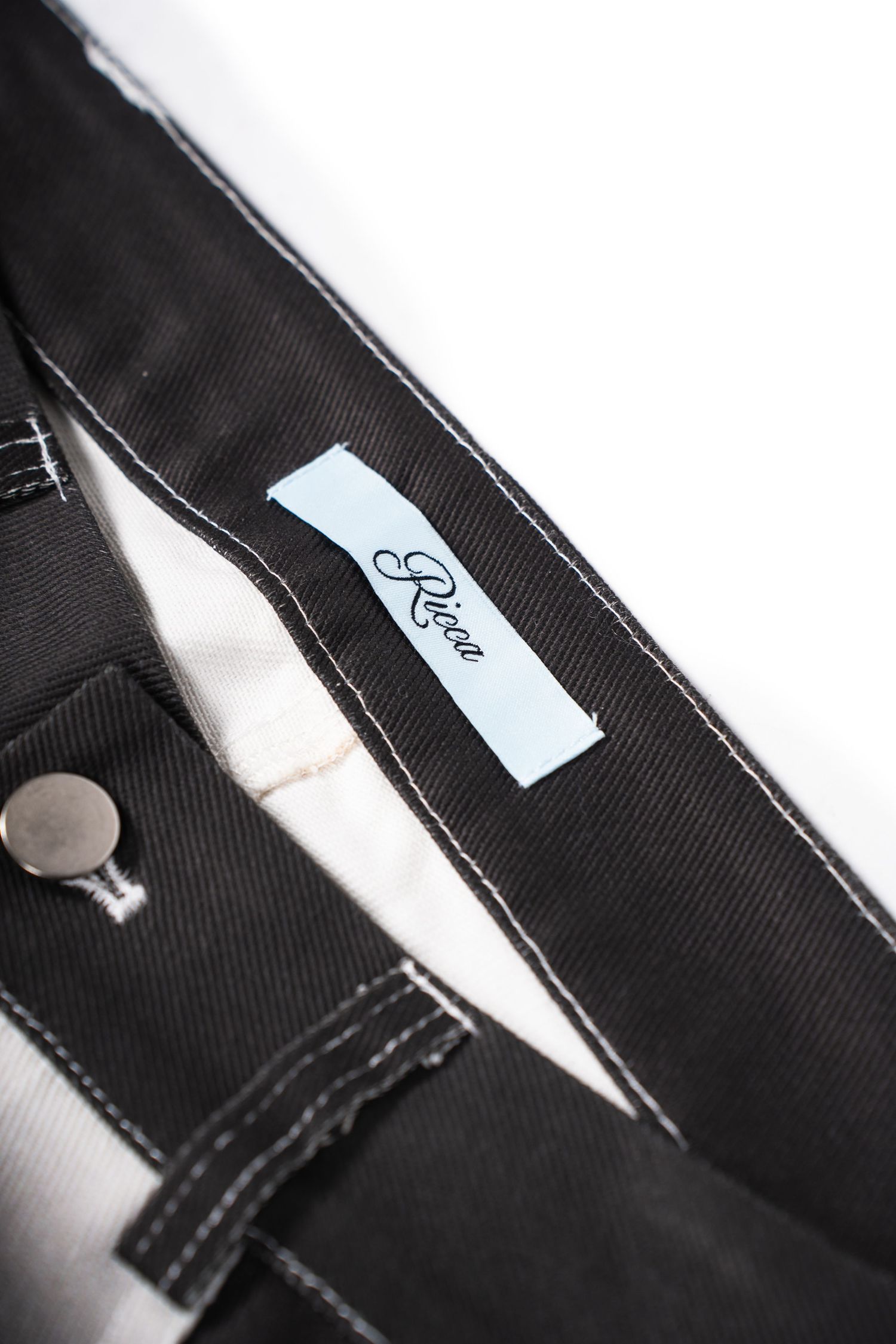 Close-up detail of black denim jeans showing white brand label and button closure.