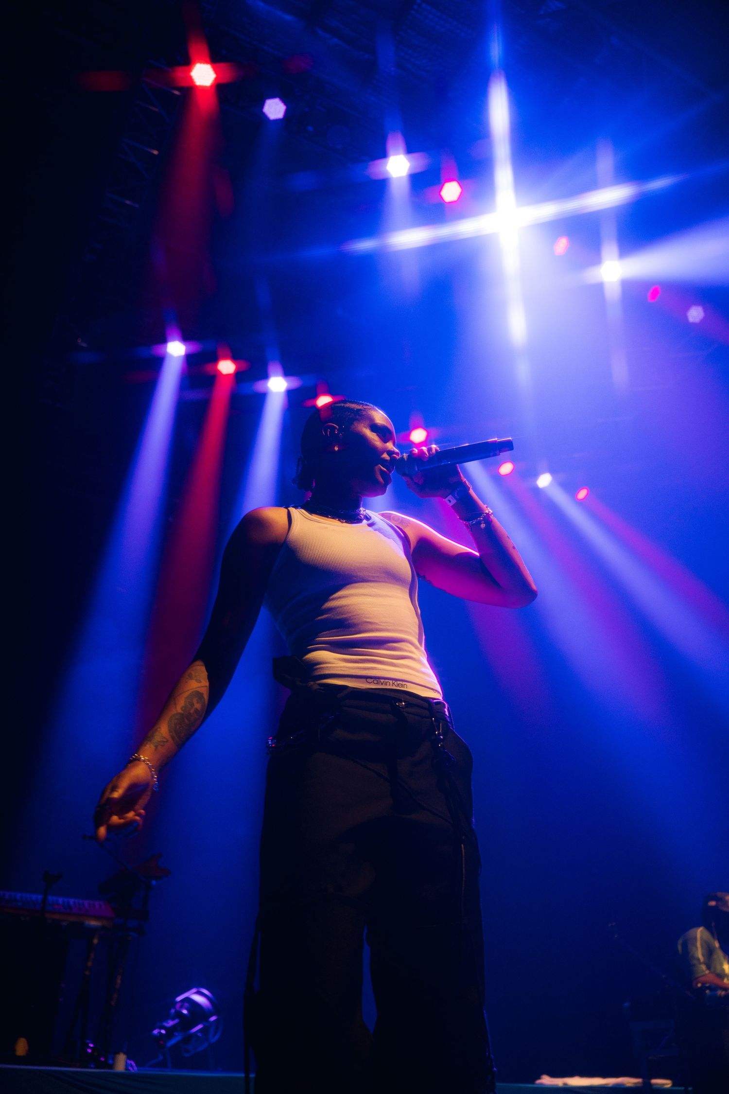 Concert performer in white tank top silhouetted against dramatic blue and red stage lighting during live performance.