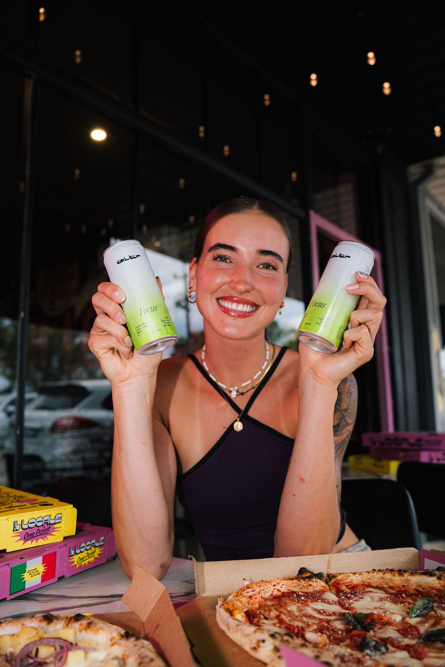 Displayed both hard seltzer drinks while sitting at a table with pizza and candy boxes in a dimly lit restaurant setting.