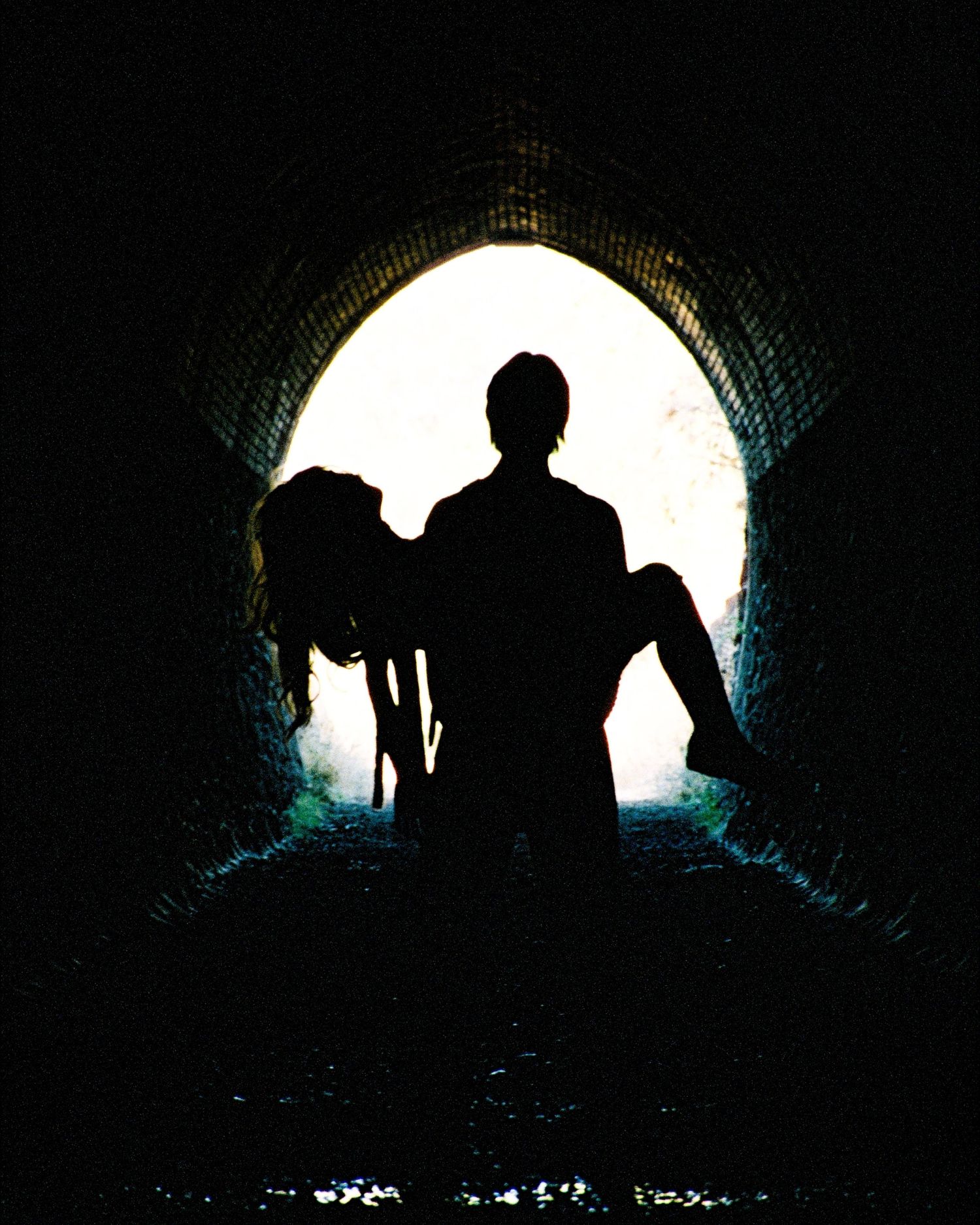 Silhouette of a figure carrying someone in a tunnel with bright backlight creating a dramatic contrast effect.
