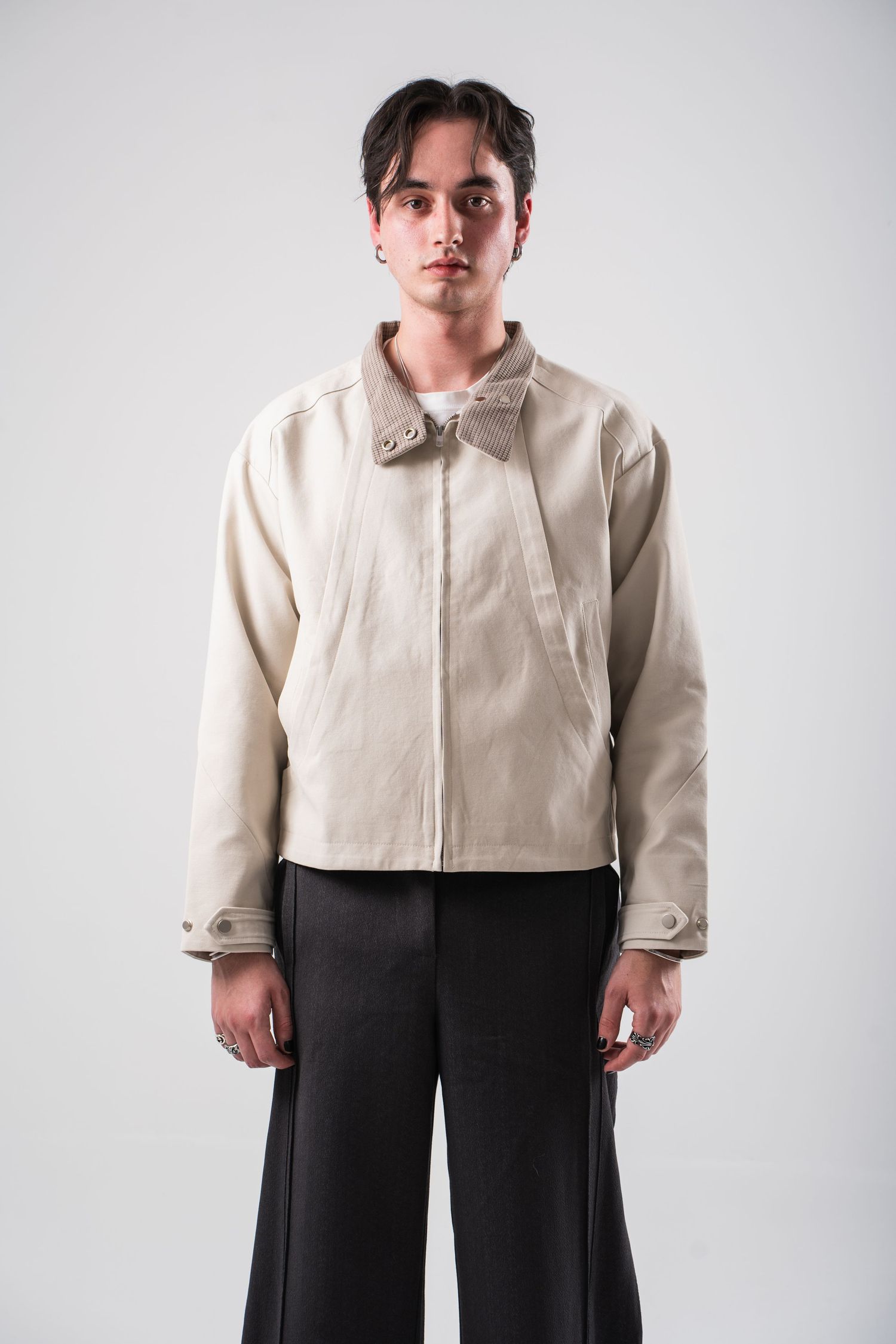 Person in beige cropped jacket and wide-leg dark trousers posing against light background in studio setting.