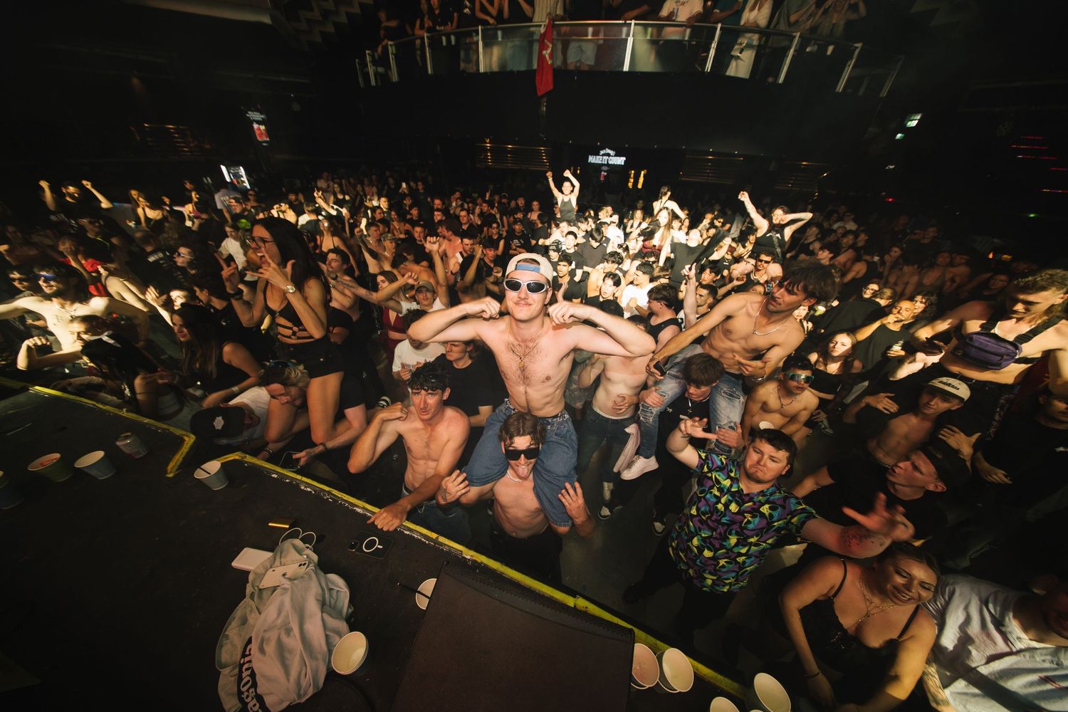 Crowded concert venue with people dancing and moshing in a dark room illuminated by stage lights.